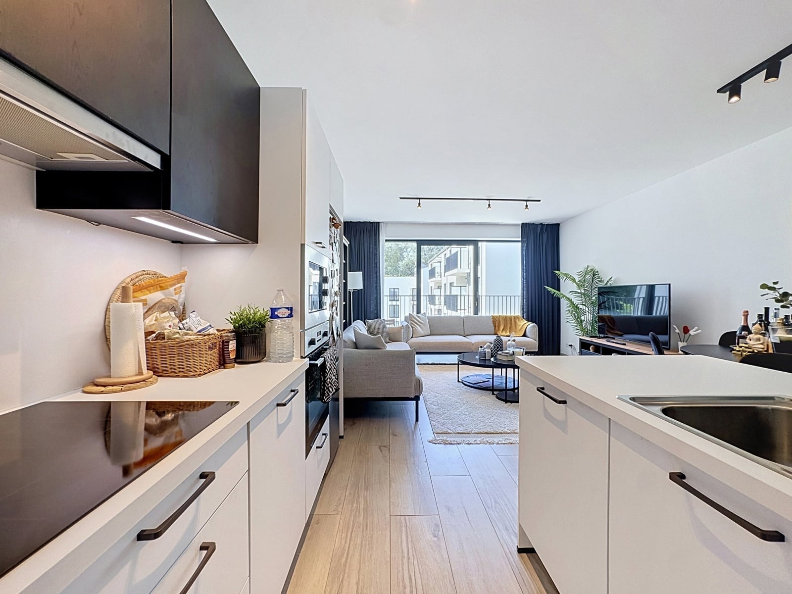 Cuisine Ouverte et Salon Lumineux – You Real Estate Agency Appartement moderne avec cuisine ouverte et salon lumineux donnant sur balcon.