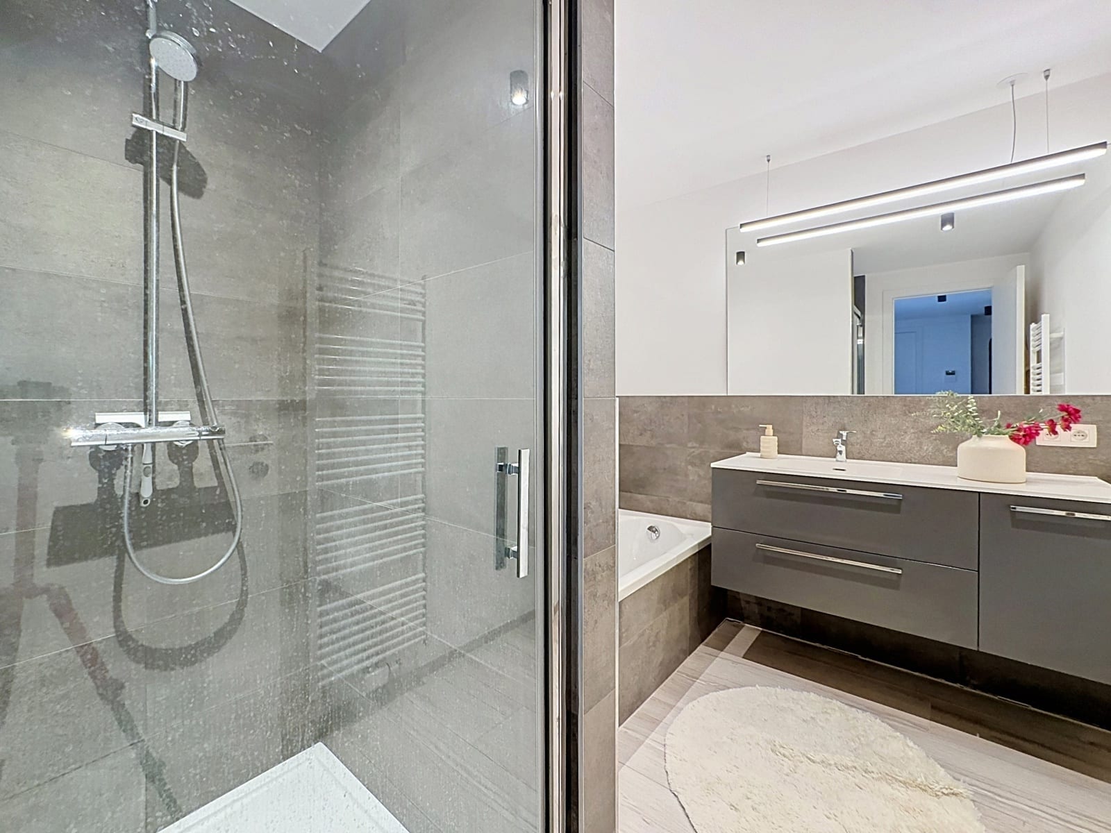 Salle de Bains Moderne – You Real Estate Agency Salle de bains moderne avec douche vitrée, meuble vasque suspendu et grand miroir.