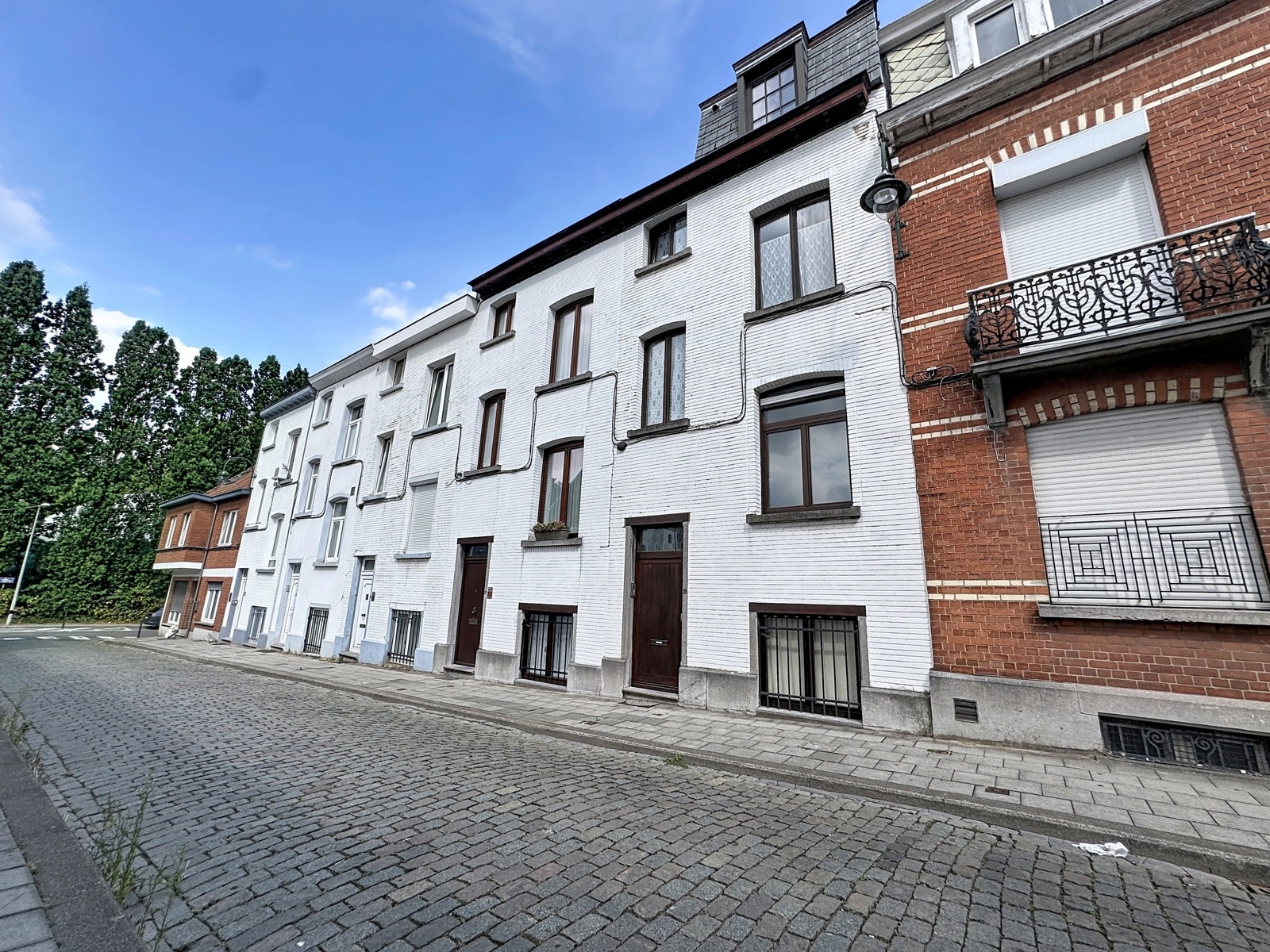 whise photo 32 Row of white brick townhouses on a cobblestone street, blue sky and tall green trees to the left.