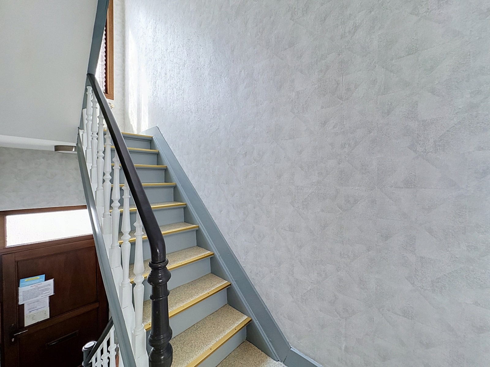 whise photo 9 Industrial-style interior staircase with grey steps, white balusters, and a black handrail beside a textured light-grey wall.
