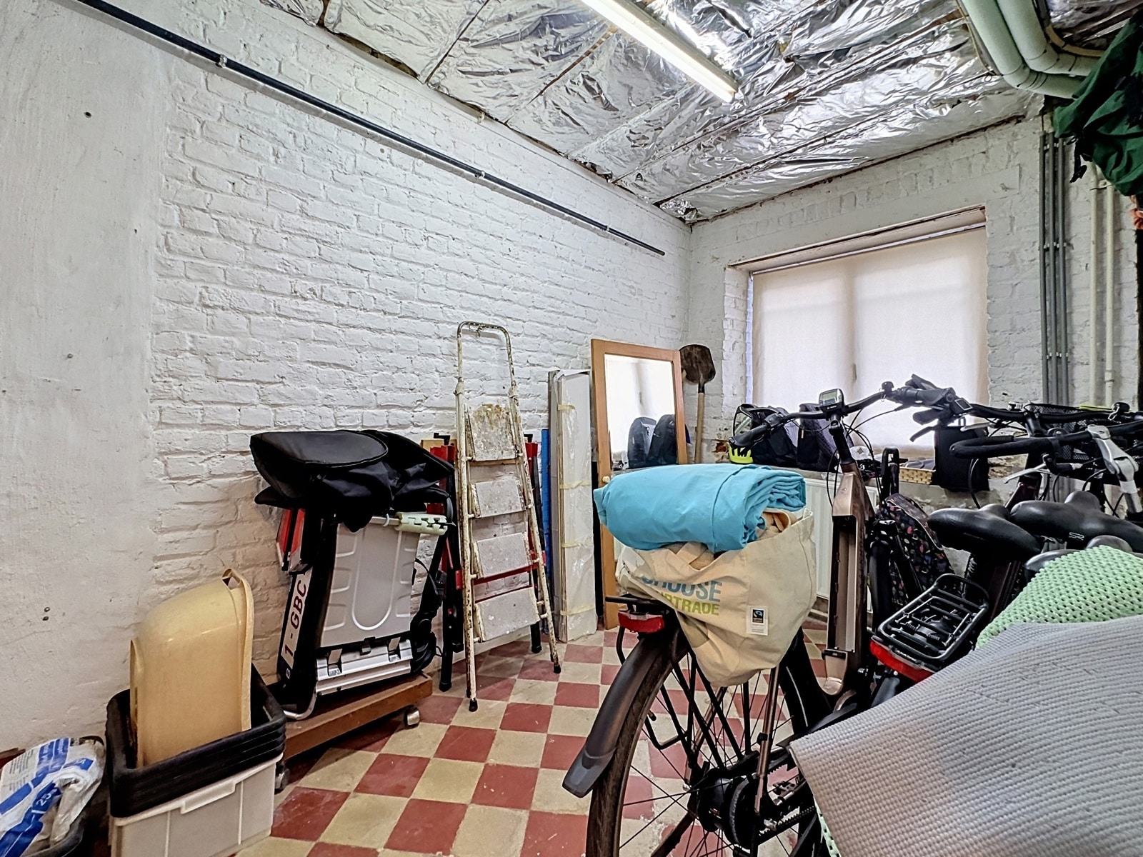 whise photo 24 Cluttered indoor storage room with two bicycles and miscellaneous gear against white brick walls and a windowed wall behind.