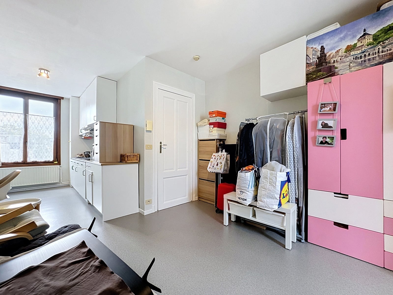 whise photo 13 Bright home room with white cabinets along left wall, a window, and a pink wardrobe filled with clothes and boxes nearby.