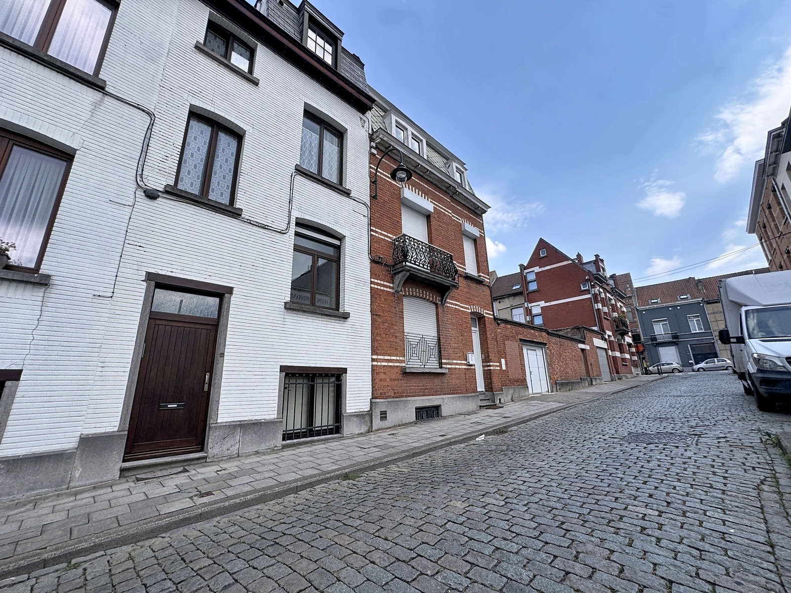whise photo 31 Cobblestone street lined with white and red brick row houses under a blue sky.