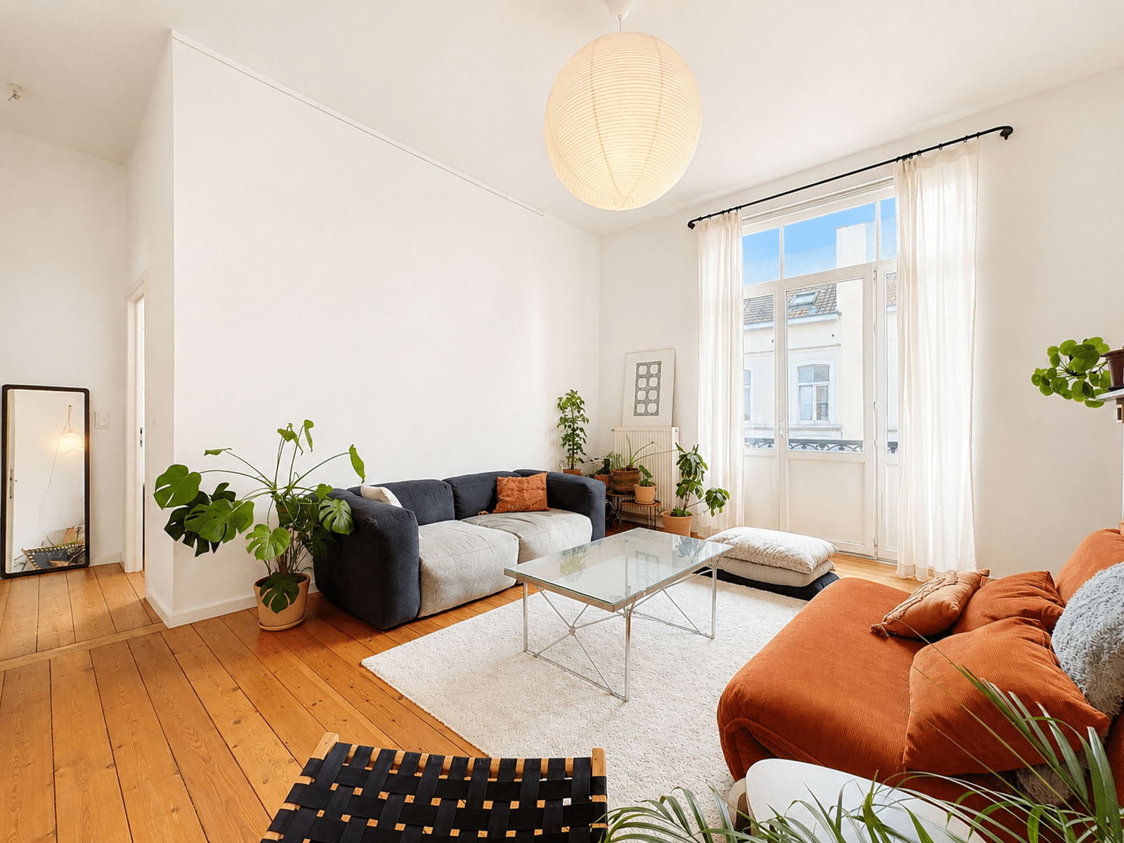 Salon Lumineux avec Canapé Terracotta – You Real Estate Agency Salon lumineux d’appartement avec hauts plafonds, parquet bois et canapé terracotta.
