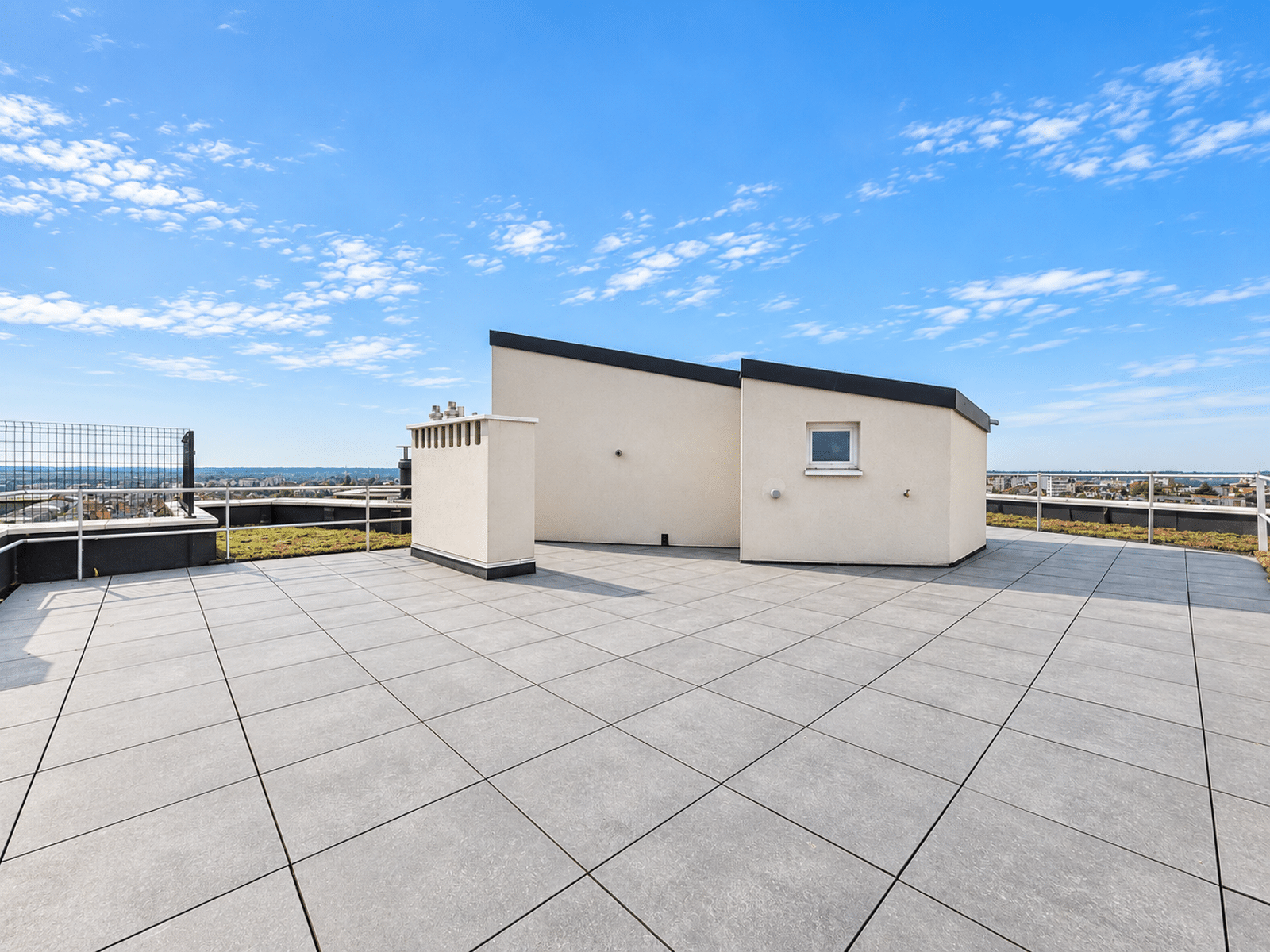 Toit-Terrasse avec Vue Urbaine – You Real Estate Agency Grande terrasse rooftop moderne avec vue urbaine et ciel dégagé.