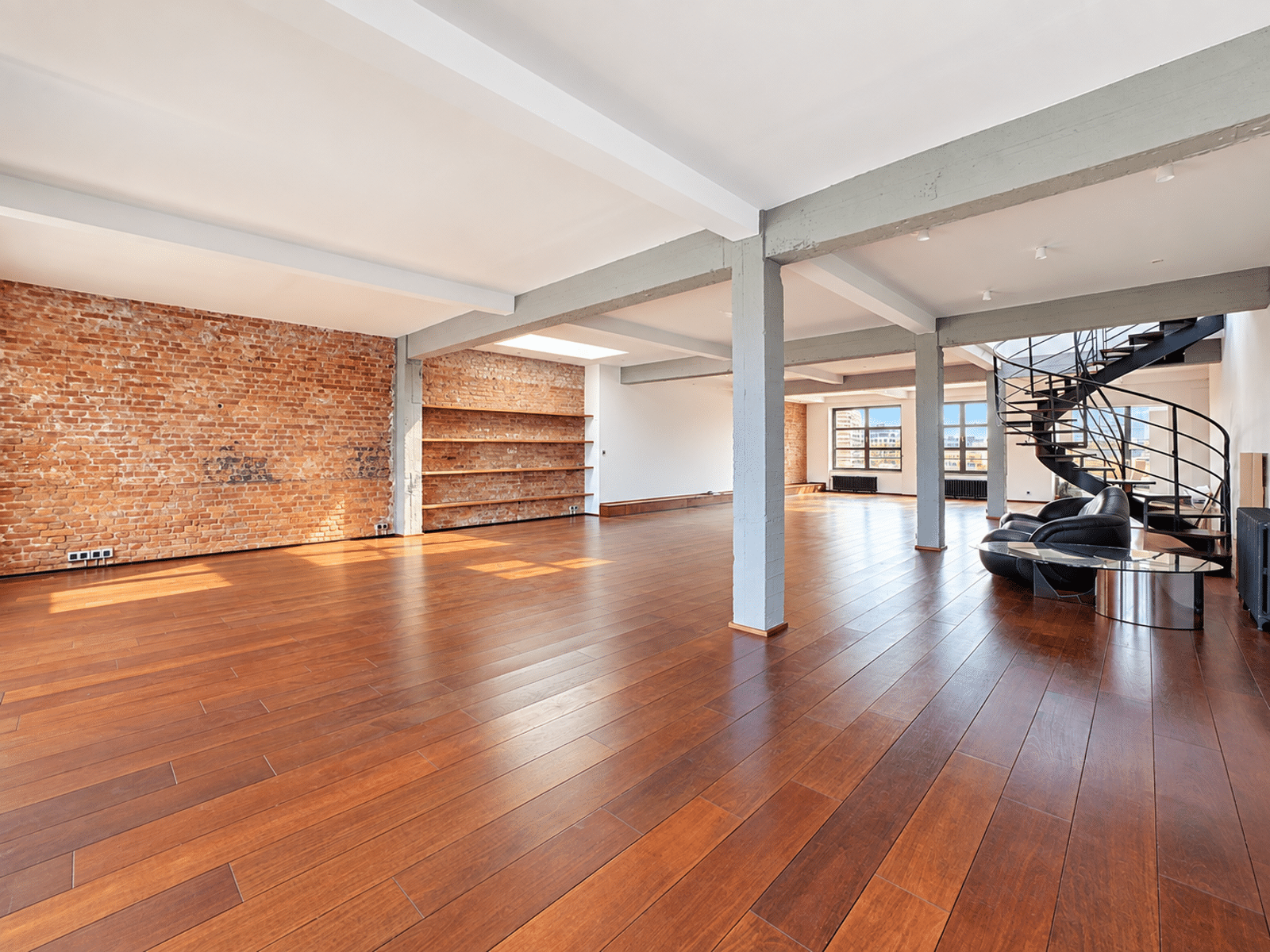 Salon Loft avec Mur en Brique – You Real Estate Agency Salon spacieux d’appartement loft avec parquet, mur en brique et escalier en colimaçon.