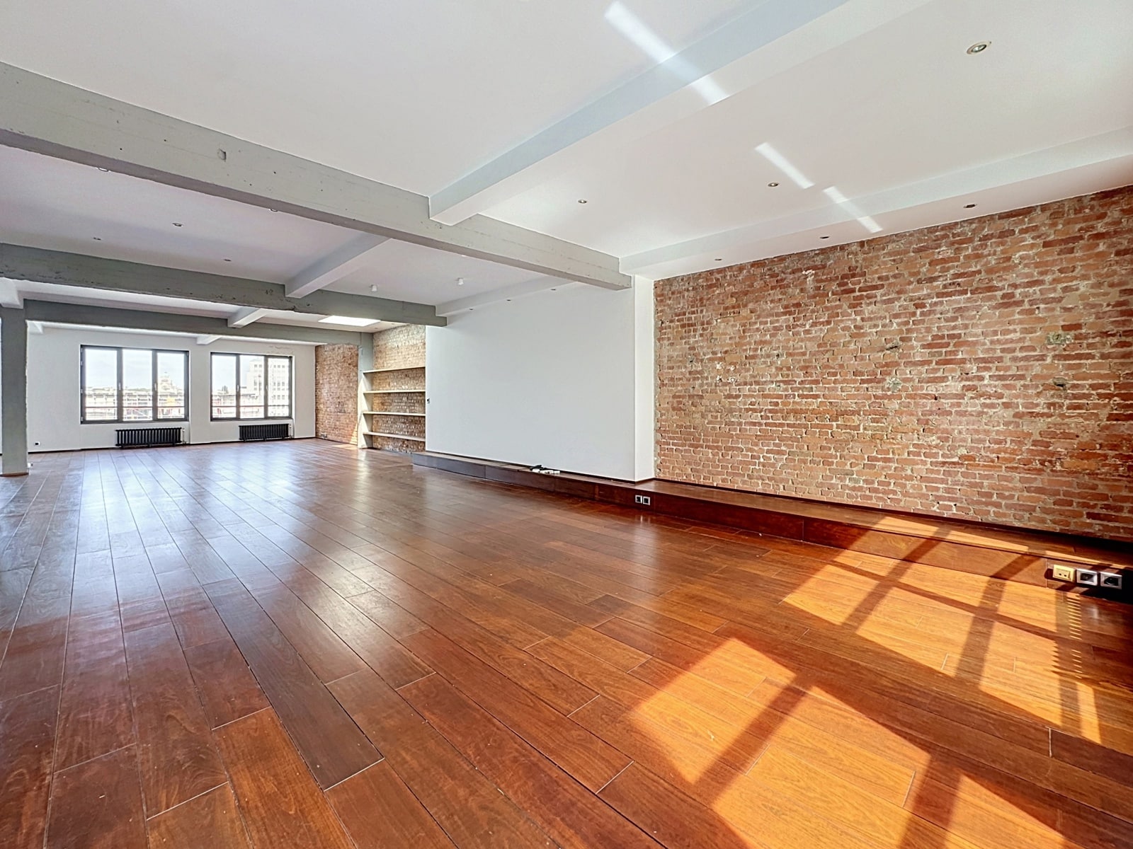 Loft Lumineux avec Mur en Briques – You Real Estate Agency Appartement loft lumineux avec parquet, mur en briques et grandes fenêtres.