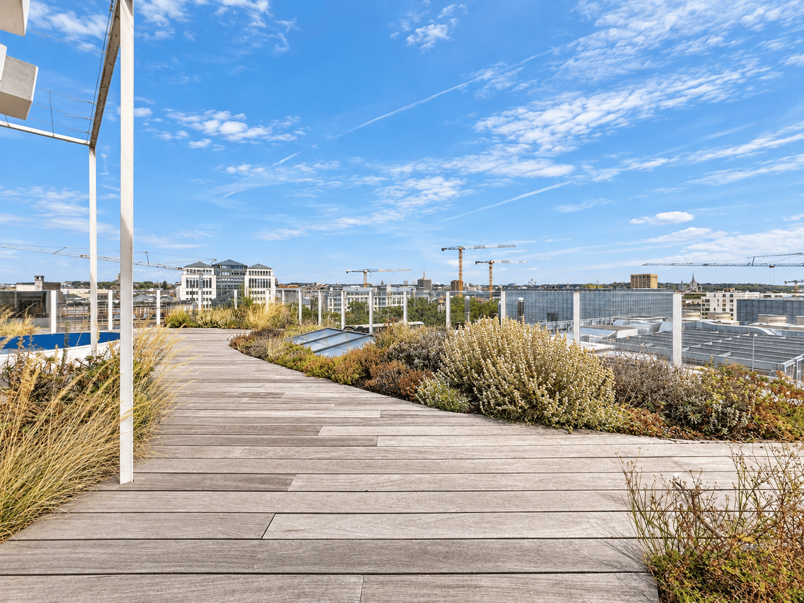 Toit-Terrasse Paysager – You Real Estate Agency Terrasse rooftop d’appartement avec jardin paysager et vue sur panorama urbain.