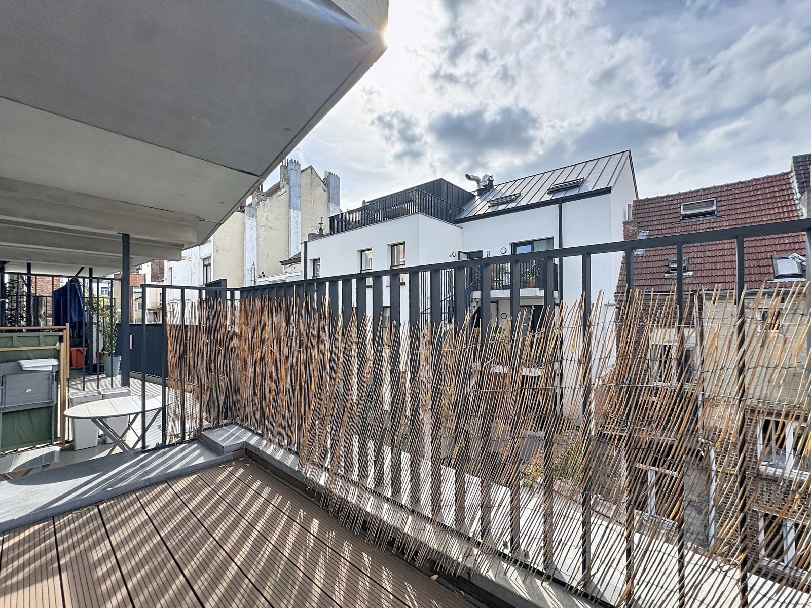Balcon Urbain avec Brise-Vue – You Real Estate Agency Terrasse d’appartement avec platelage bois, brise-vue bambou et vue urbaine.