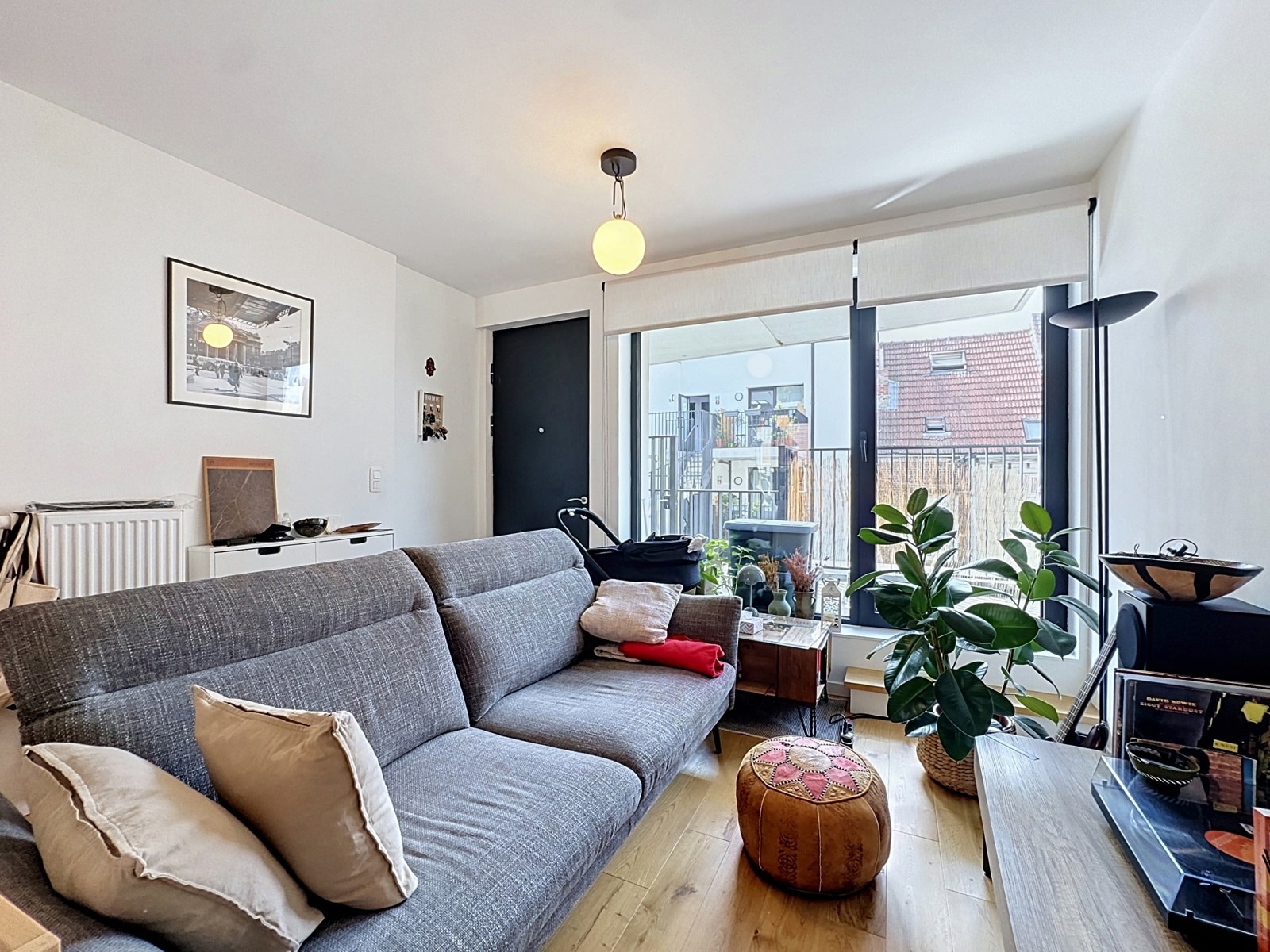 whise photo 4 Cozy living room with a gray fabric sofa, beige cushions, and a round leather pouf on a wooden floor.