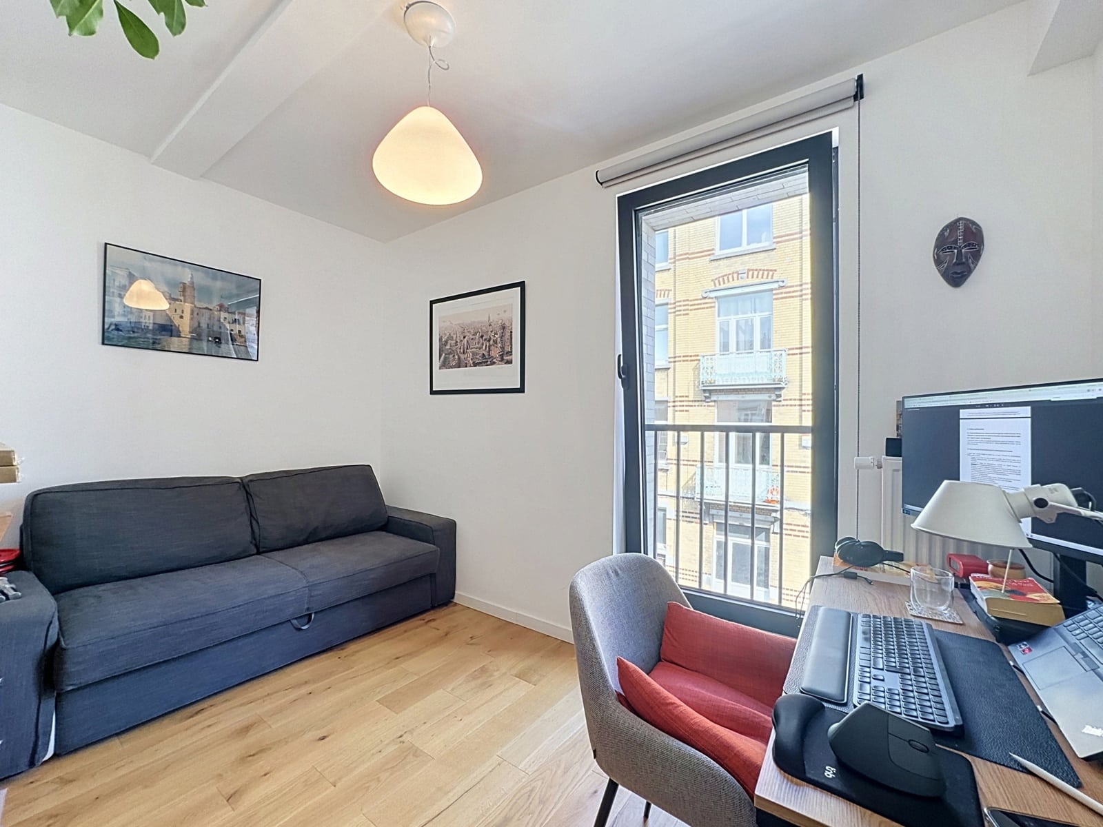 whise photo 17 Cozy office living room with gray sofa, wood floor, two framed photos on white walls, and a large window letting in daylight.