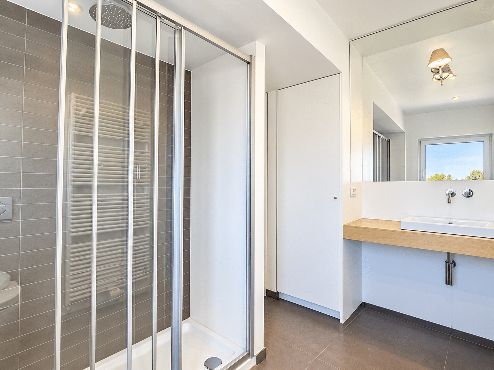 Salle de Bain avec Douche Vitrée – You Real Estate Agency Salle de bain moderne d’appartement avec douche vitrée, vasque blanche et miroir.