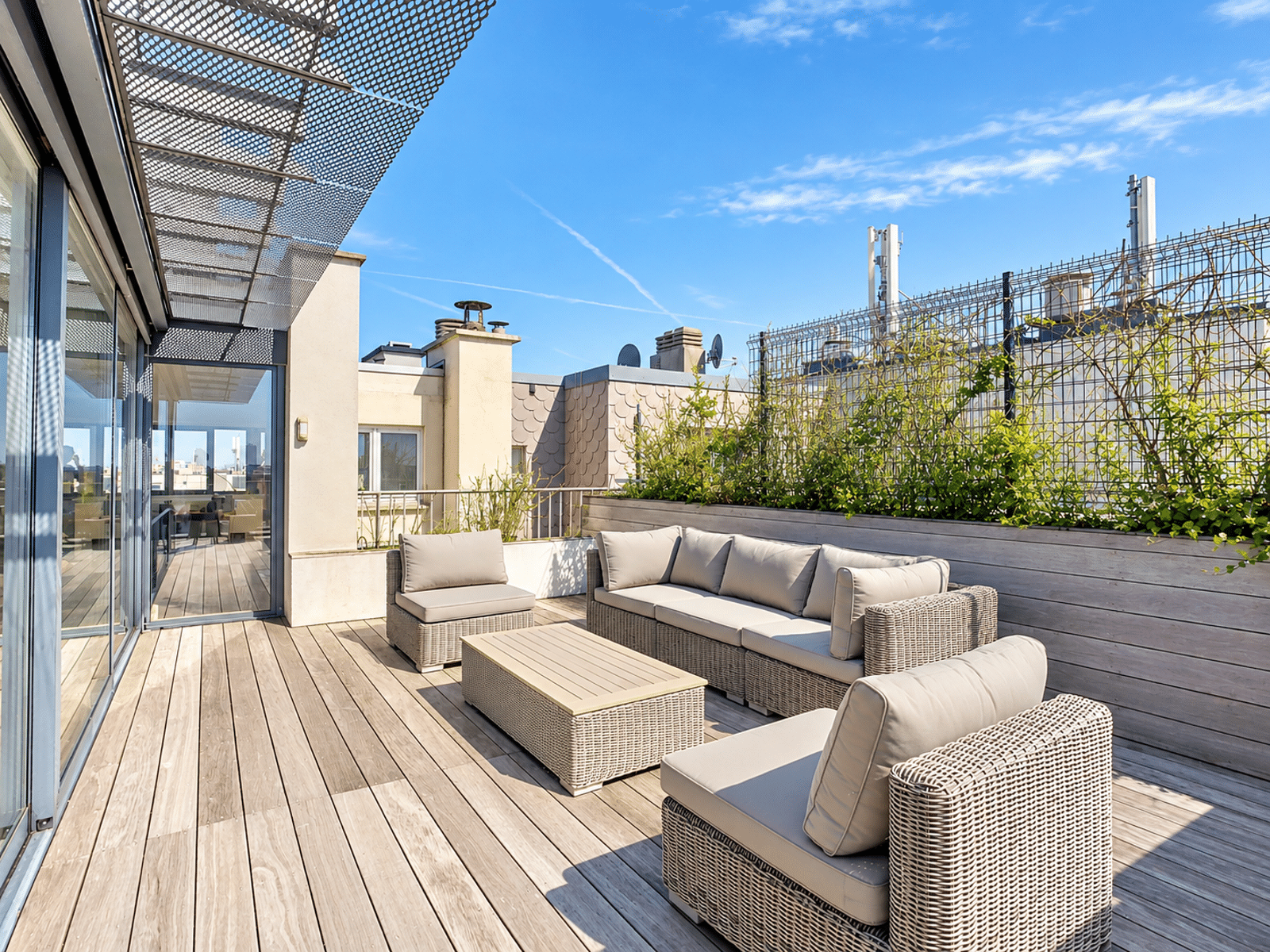Terrasse Rooftop avec Salon Extérieur – You Real Estate Agency Terrasse rooftop d’appartement avec salon extérieur en rotin et jardinières végétalisées.