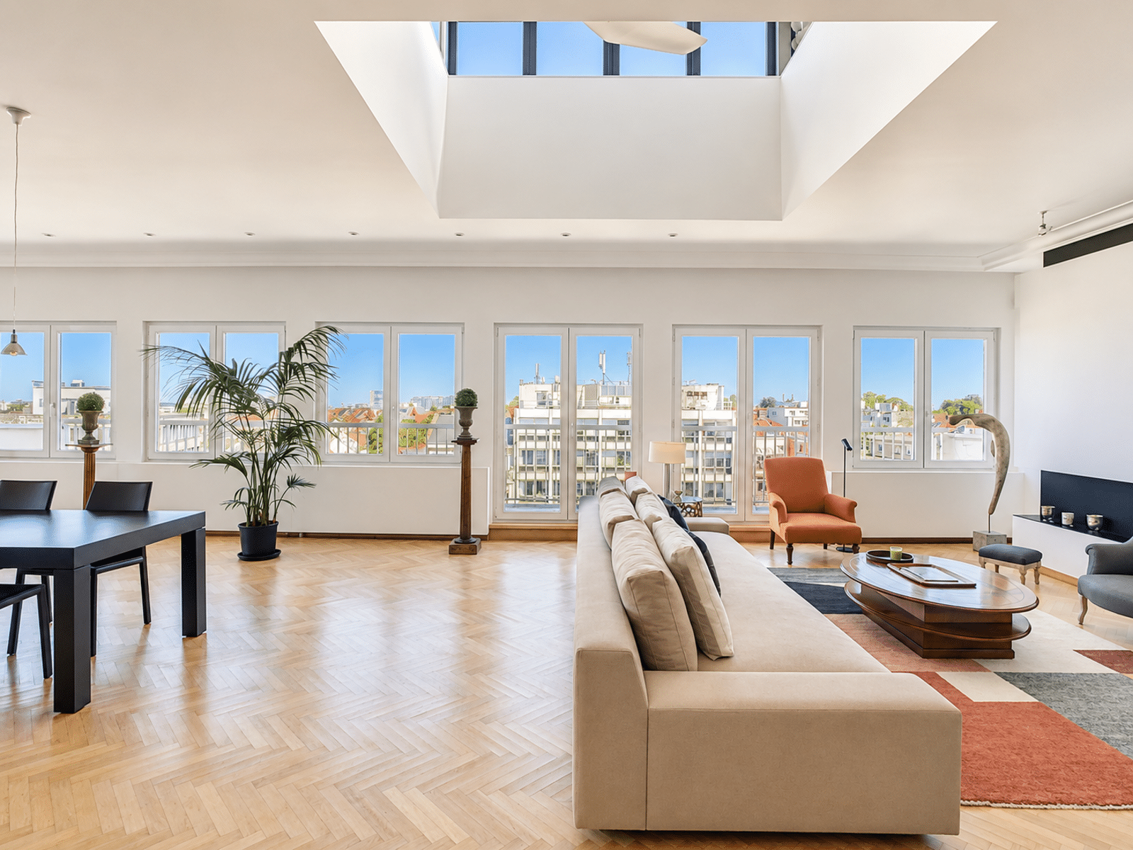 whise photo 3 Bright open-plan living room with beige sofa, orange armchair, hardwood floor and large windows overlooking cityscape.