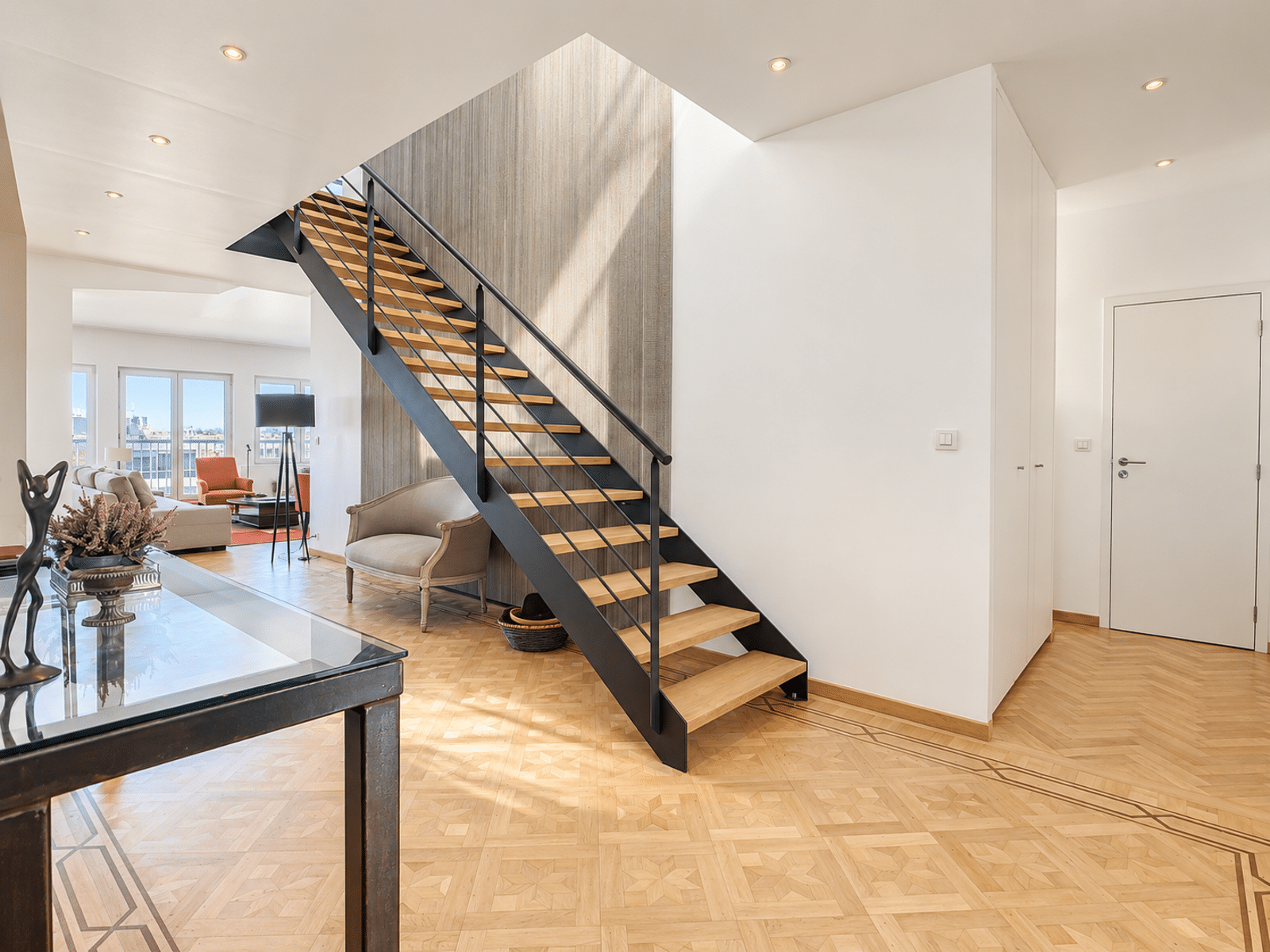 Escalier Ouvert et Parquet Géométrique – You Real Estate Agency Intérieur de maison moderne avec escalier ouvert, parquet géométrique et salon lumineux.