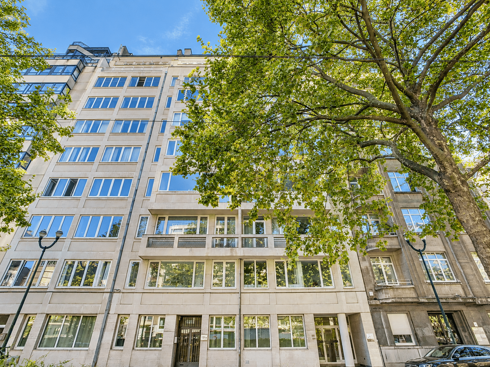 Façade d’Immeuble Résidentiel – You Real Estate Agency Immeuble résidentiel moderne avec appartements et balcon, façade claire en rue arborée.