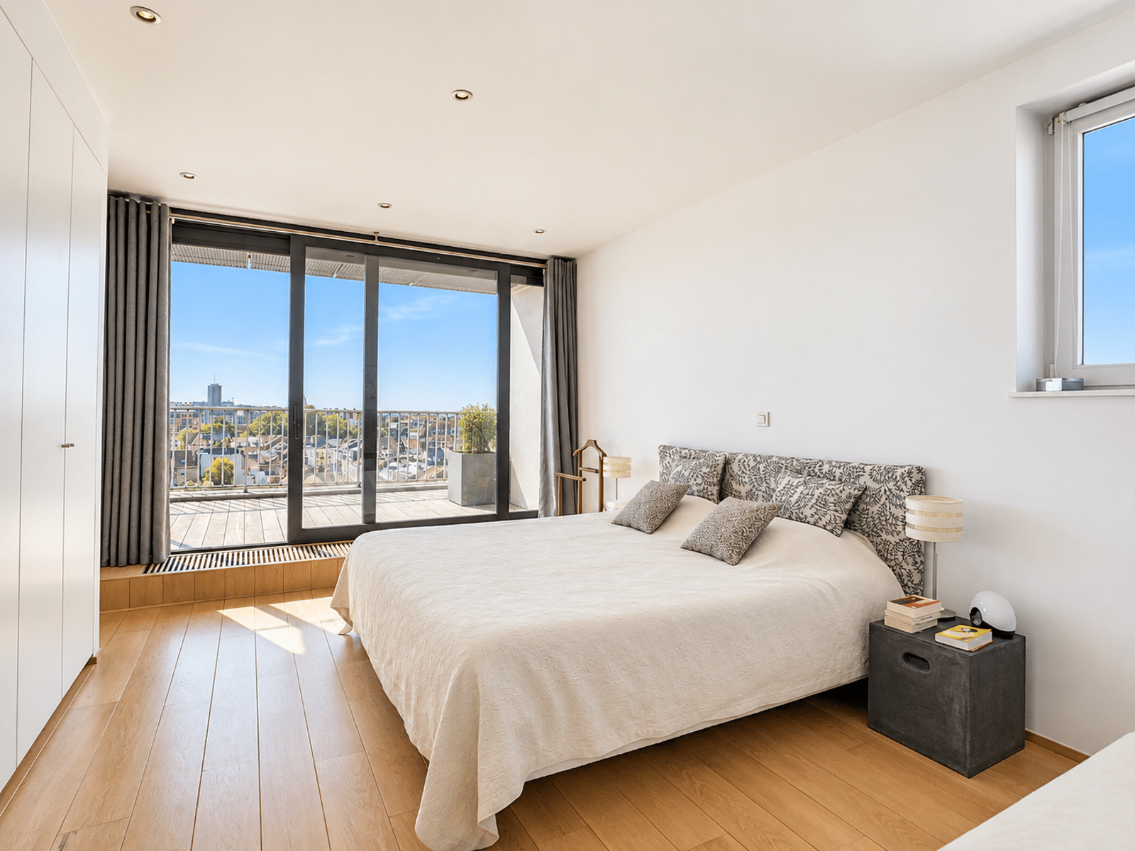 Chambre Lumineuse avec Balcon – You Real Estate Agency Chambre moderne d’appartement avec balcon et vue urbaine lumineuse.