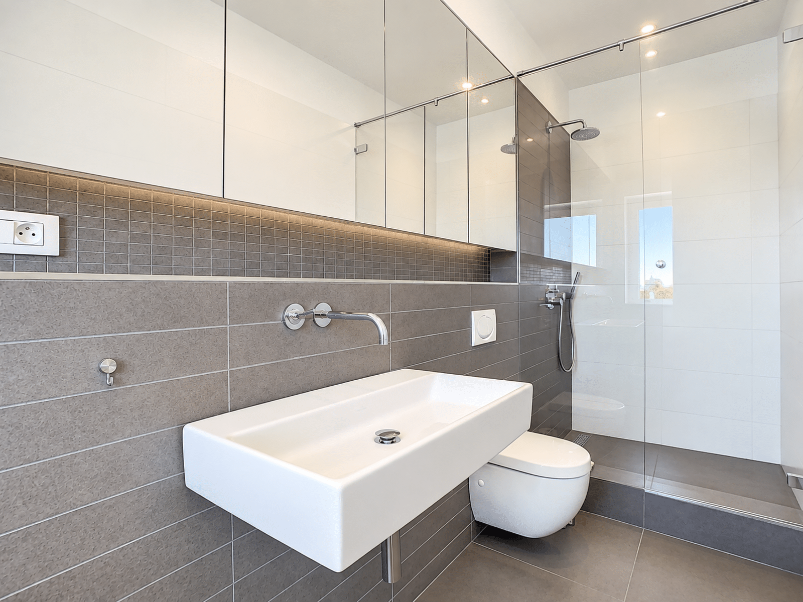 Salle de Bain Moderne avec Douche – You Real Estate Agency Salle de bain moderne d’appartement avec douche italienne, vasque et toilettes suspendues.