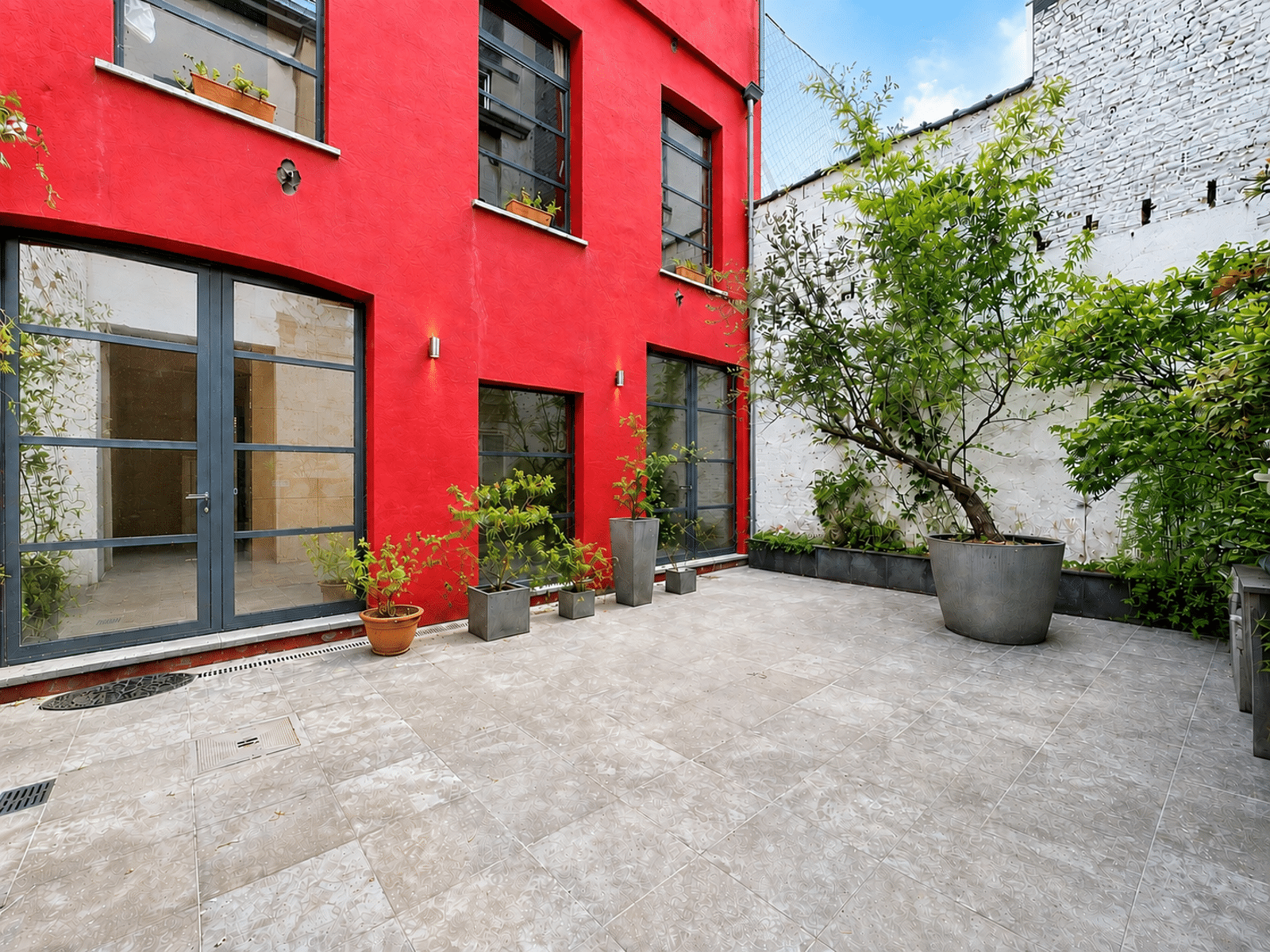 whise photo 18 Red-painted building courtyard with large glass doors, concrete tiles, and a variety of potted plants along the wall.