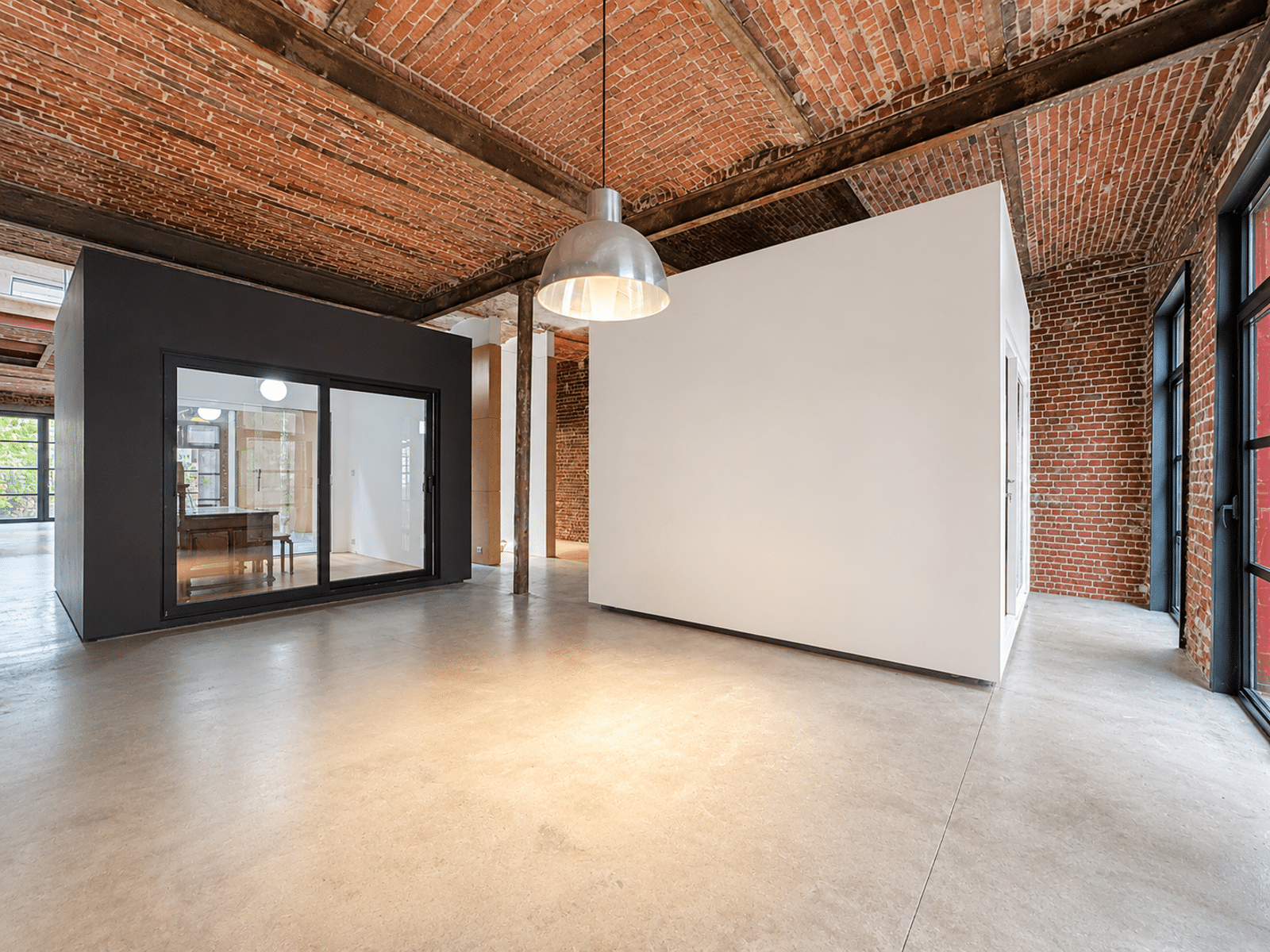 Salon de Loft Industriel Rénové – You Real Estate Agency Salon de loft industriel rénové avec plafond voûté en briques et volumes modernes.