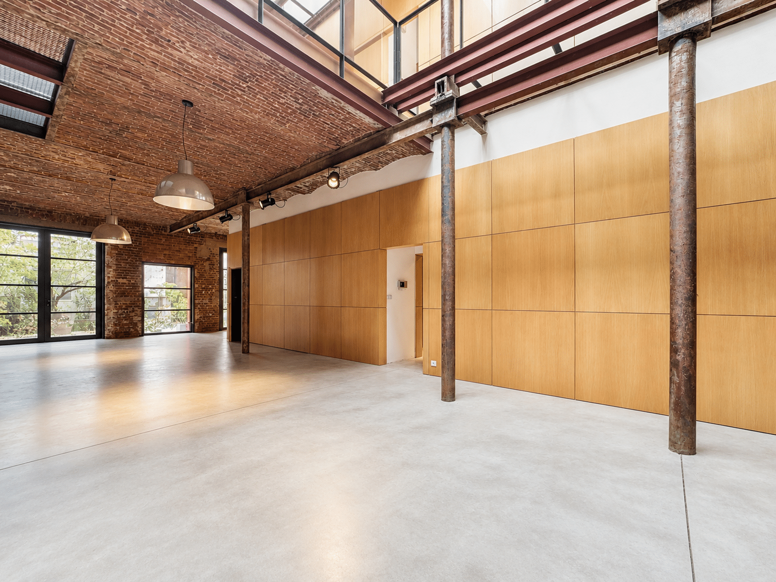 Salon Loft Industriel avec Briques – You Real Estate Agency Salon loft industriel spacieux avec briques apparentes, verrière, poutres métalliques et sol béton.