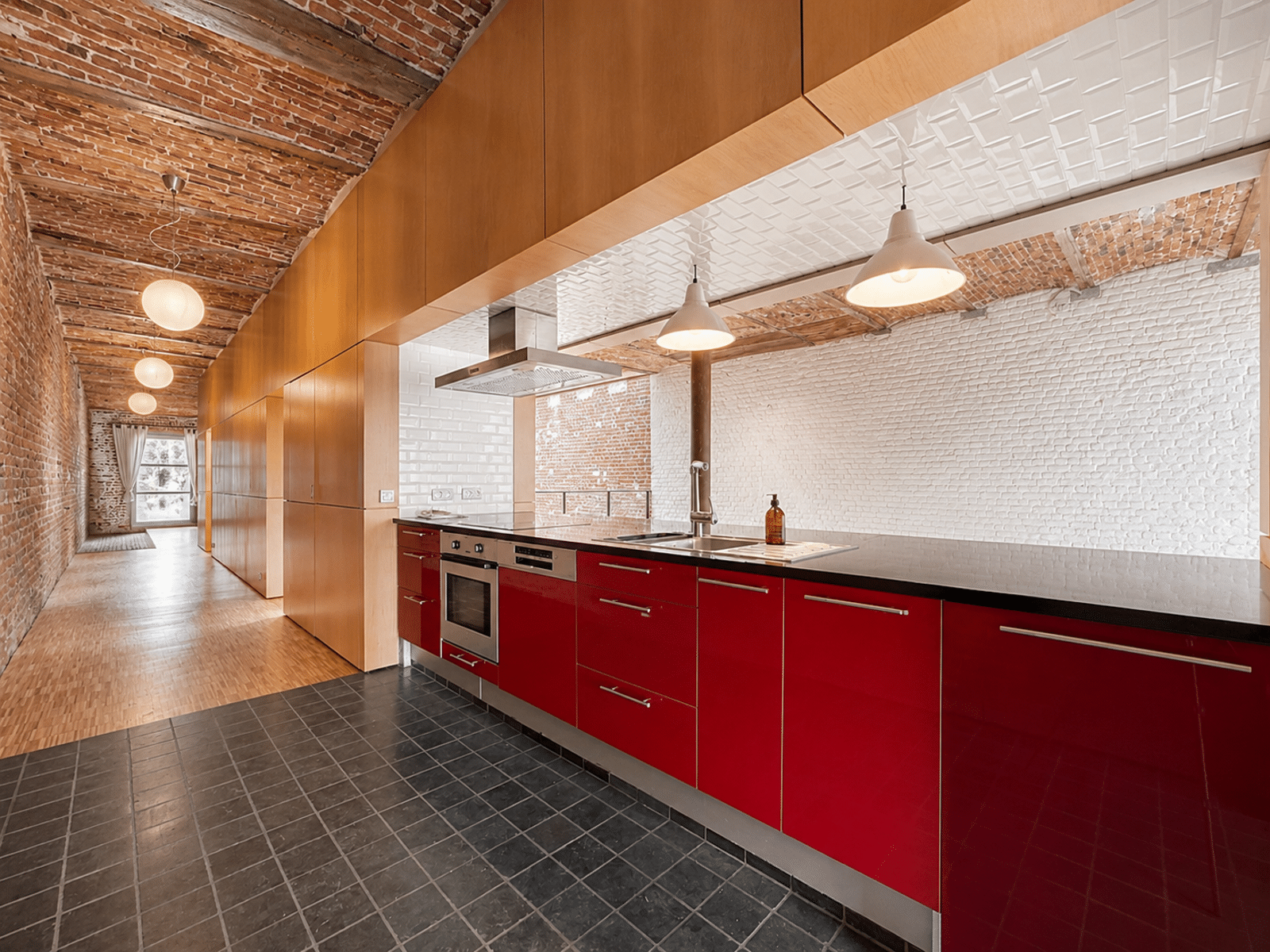 Cuisine Rouge Moderne Style Loft – You Real Estate Agency Cuisine moderne rouge dans appartement loft avec briques apparentes et poutres.