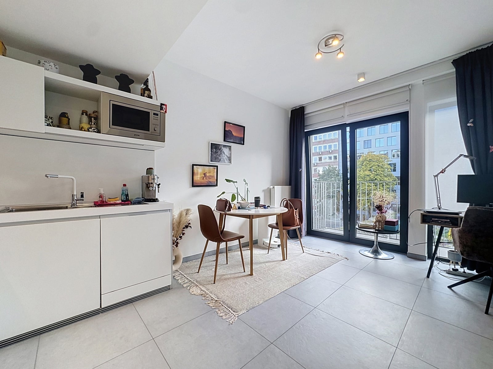 whise photo 4 Bright, open-plan kitchen and dining area with white cabinetry, microwave, and a small round table set for two near a balcony door.