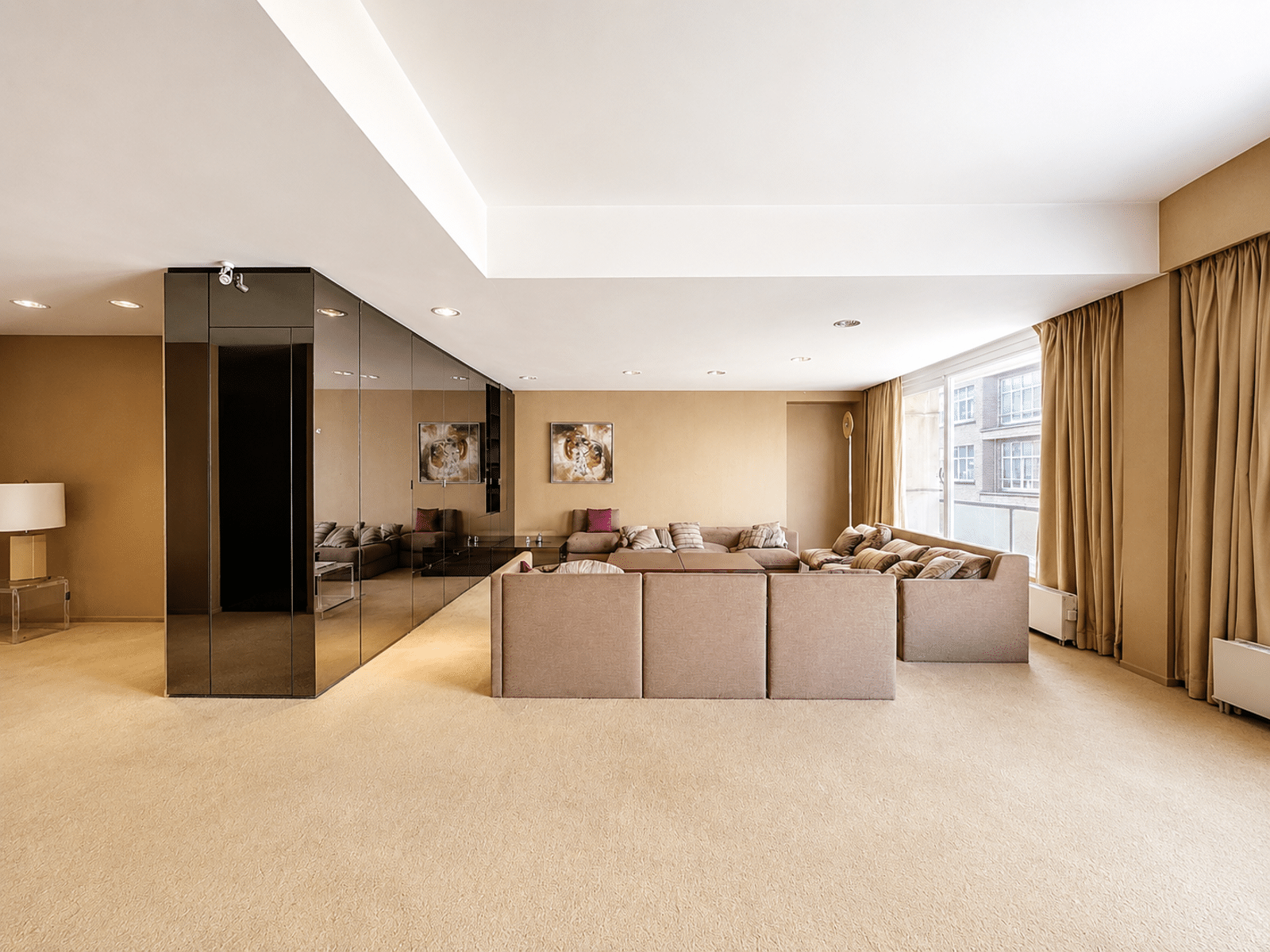 Elegante en lichte beige woonkamer – You Real Estate Agency Ruime en lichte woonkamer in een appartement, elegant beige interieur met grote ramen.