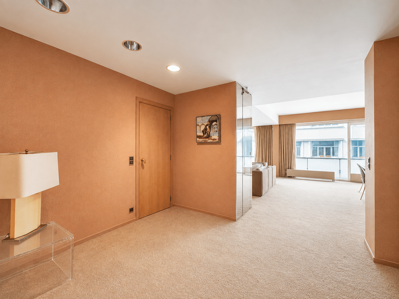 Lichte hal met toegang tot de woonkamer – You Real Estate Agency Lichte hal die uitkomt op de woonkamer met grote ramen en gordijnen.