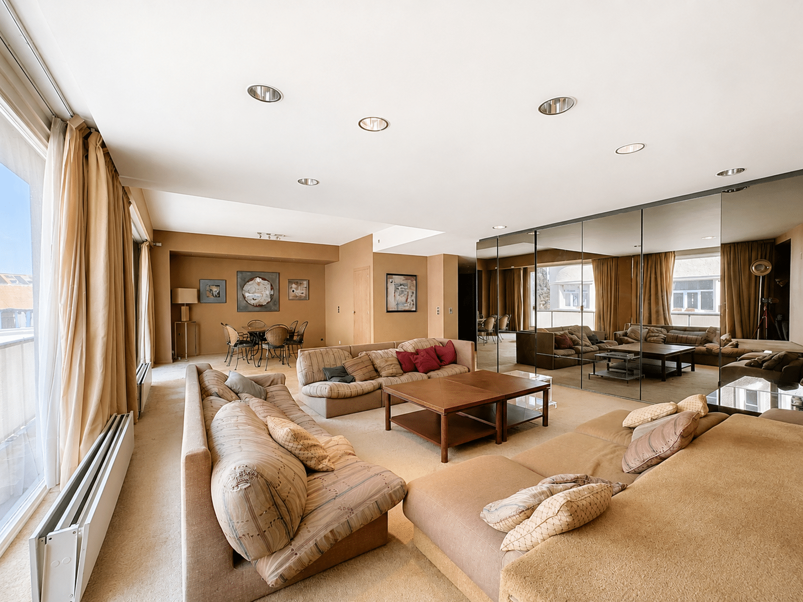 Grote, lichte woonkamer met spiegels – You Real Estate Agency Grote, lichte woonkamer in een appartement met beige banken, spiegels en een eethoek.