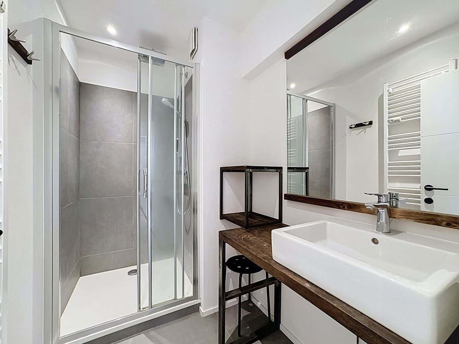 whise photo 7 Modern bathroom with glass shower enclosure, gray tile walls, white sink on a dark wood vanity, and a large mirror.