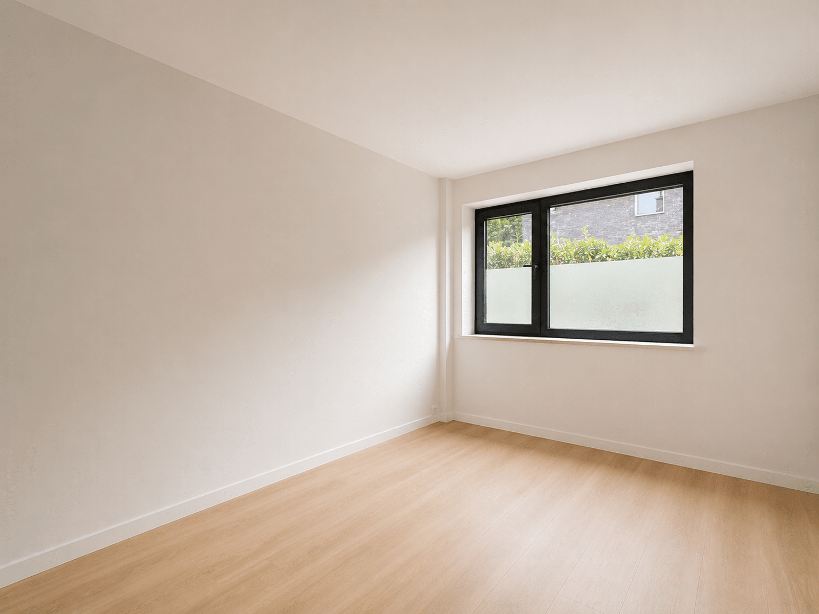 whise photo 6 Empty sunlit room with light wood flooring and a large black-framed window showing greenery outside; minimal decor.