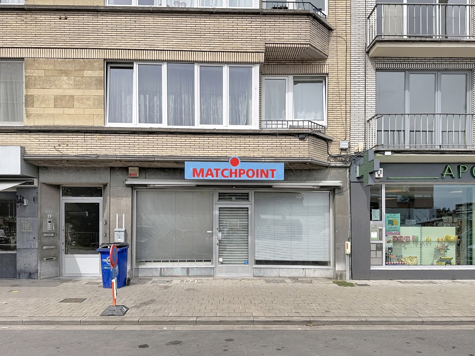 Façade Commerciale Fermée – You Real Estate Agency Rez-de-chaussée commercial fermé avec façade vitrée sous appartements en immeuble urbain.
