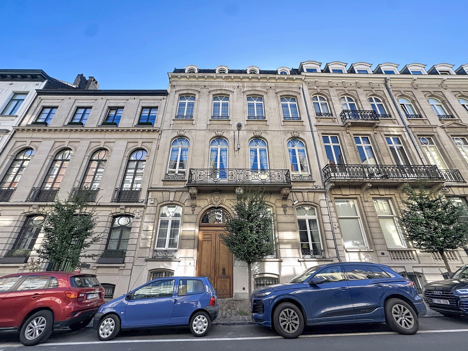 whise photo 17 Row of elegant stone townhouses with arched windows and decorative iron balconies on a sunny city street, blue sky above.