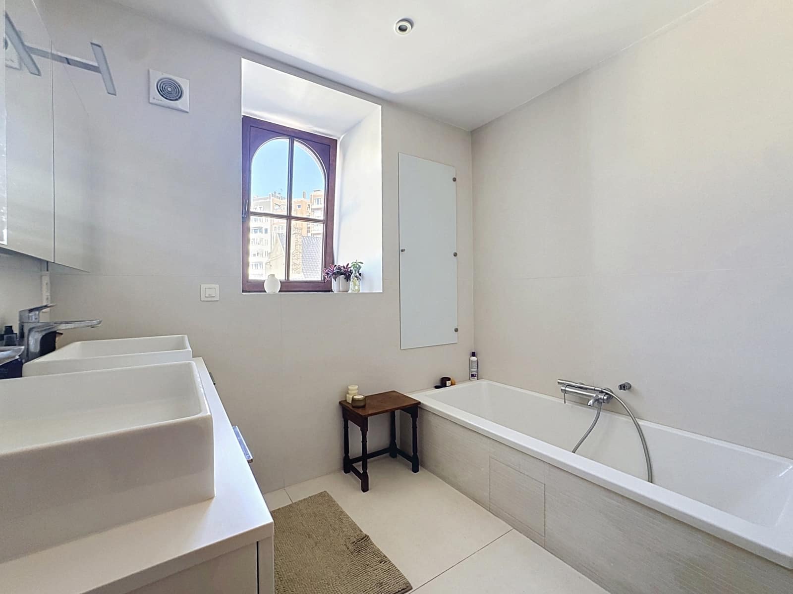 Salle de Bain Moderne et Lumineuse – You Real Estate Agency Salle de bain moderne avec baignoire, double vasque et fenêtre dans appartement lumineux.