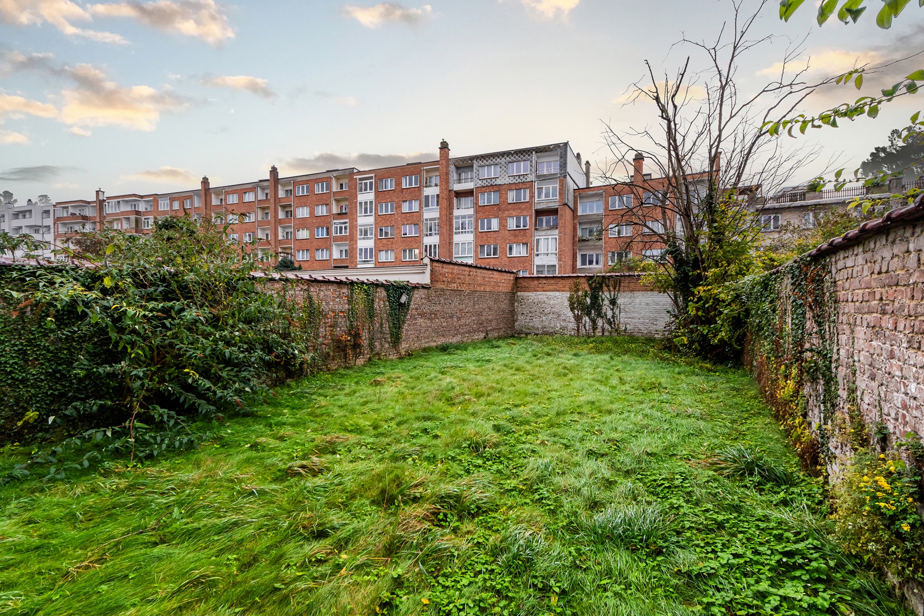Lush Private Garden – You Real Estate Agency A lush private garden at the base of a brick apartment building.
