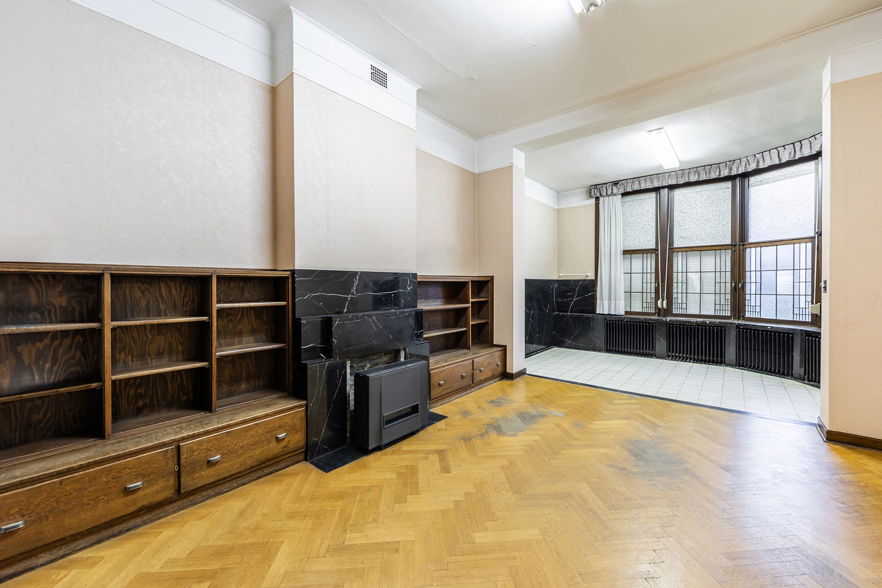Spacious Living Room with Hardwood Floors and a Fireplace – You Real Estate Agency Spacious, empty living room with hardwood floors, a marble fireplace, and built-in storage.