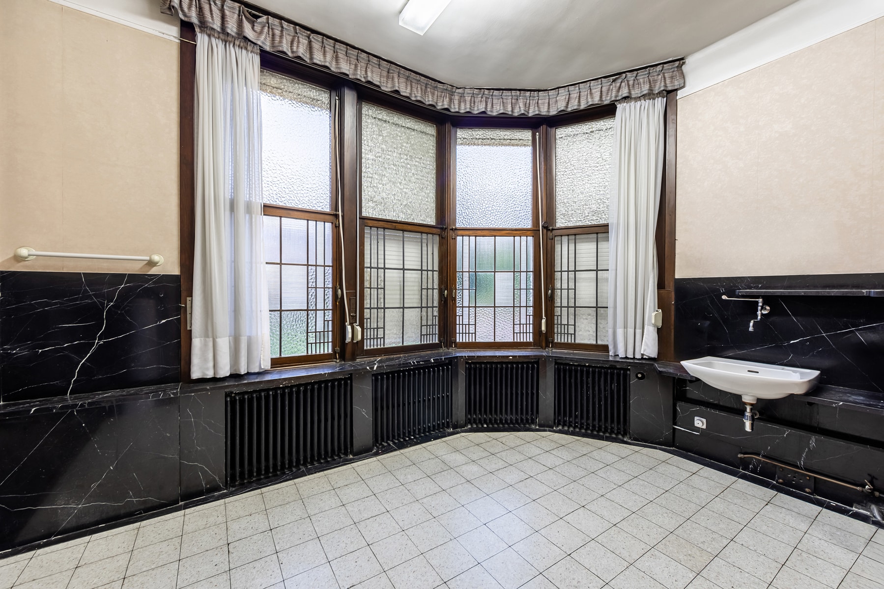 Room with a Bay Window and Black Marble – You Real Estate Agency A bright apartment room with a curved picture window, black marble, and a sink.