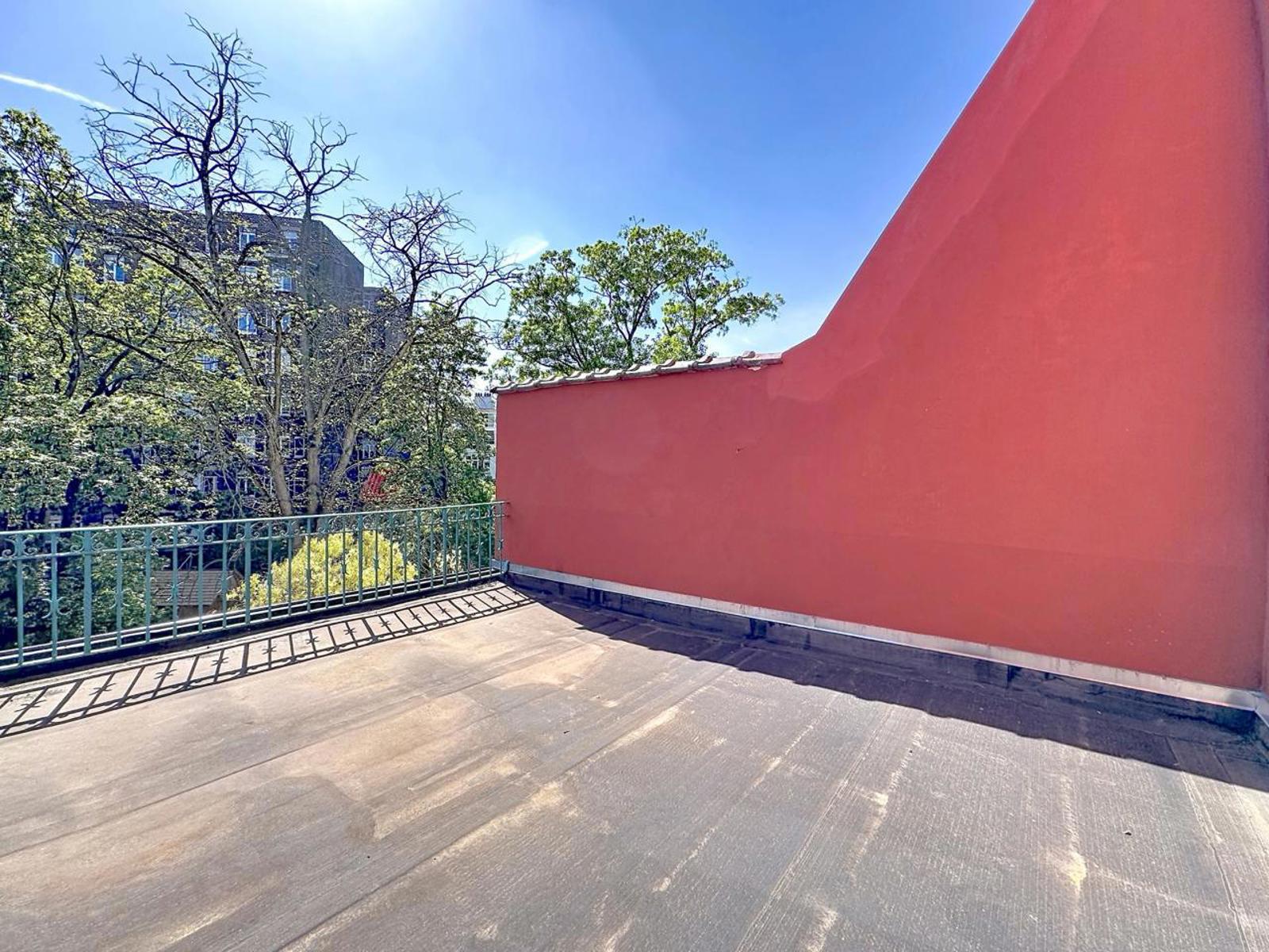 whise photo 15 Rooftop terrace with a pink stucco wall, metal railing, and concrete floor under a bright blue sky.