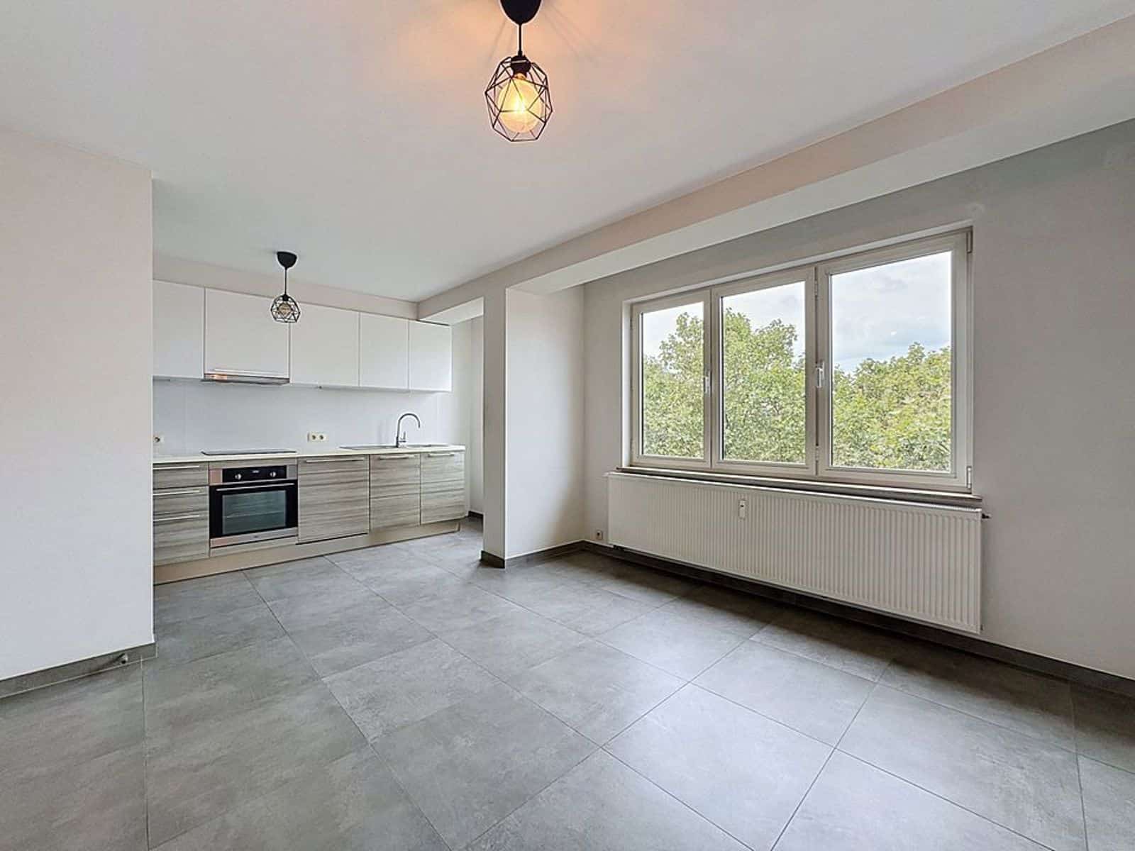 whise photo 3 Bright, empty kitchen with white upper cabinets, wood-grain lower cabinets, stainless oven, and a large window showing greenery outside.