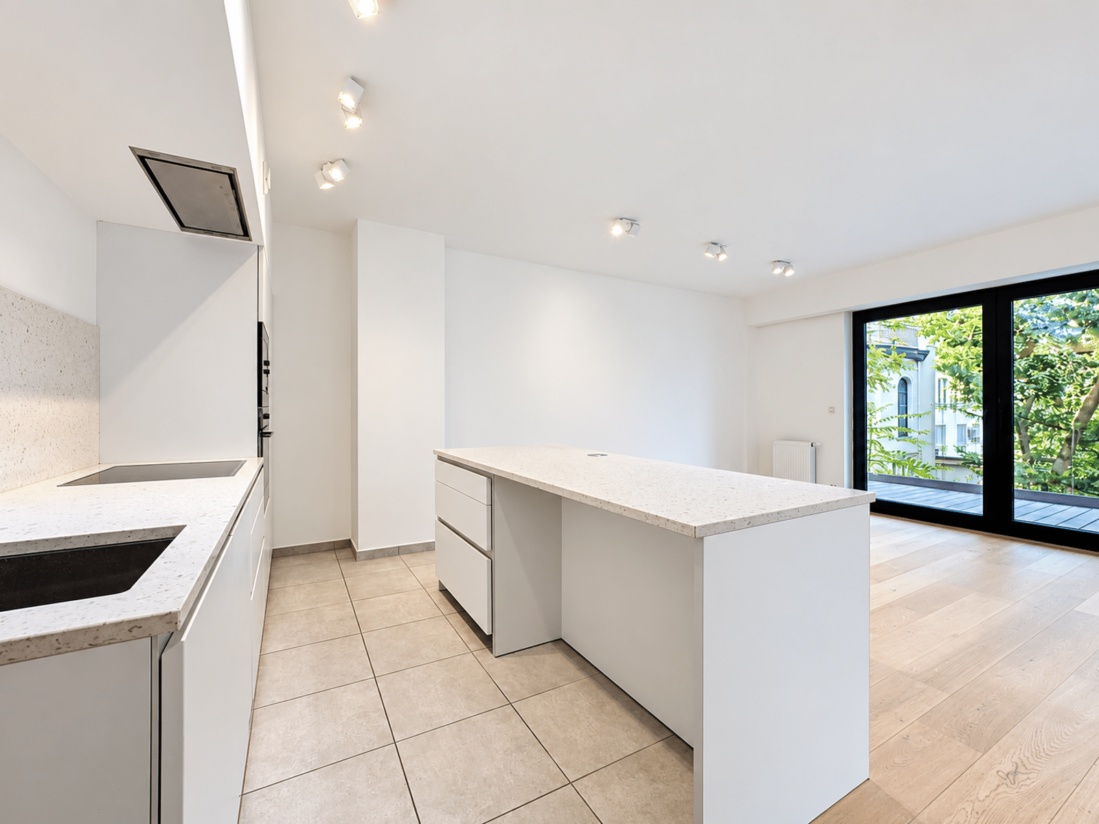 Cuisine Ouverte avec Îlot Central – You Real Estate Agency Cuisine ouverte moderne avec îlot central, salon lumineux et terrasse vitrée.