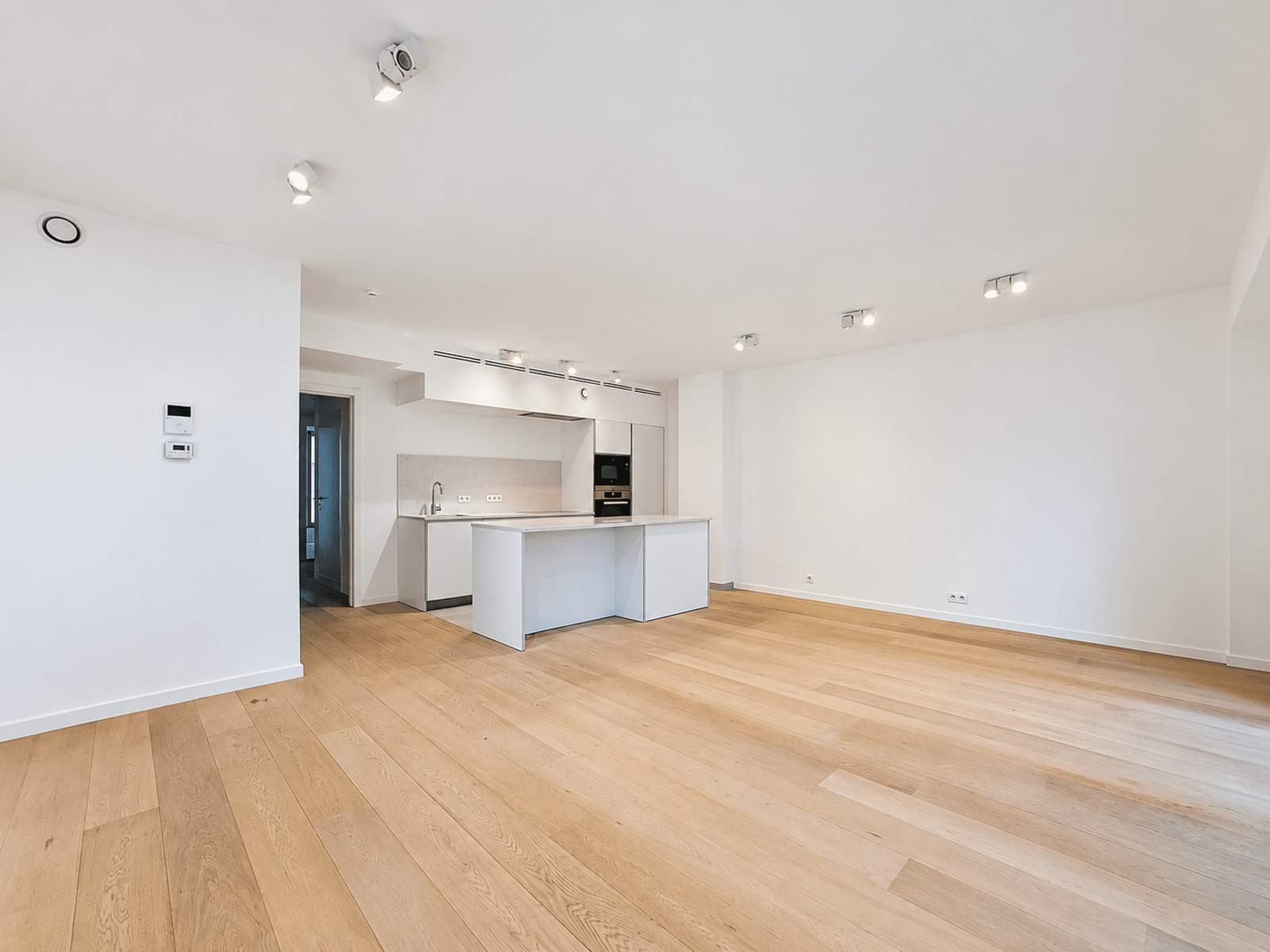 whise photo 2 Bright, empty kitchen with white cabinetry and an island, set in a room with light wood floors and ample natural lighting.