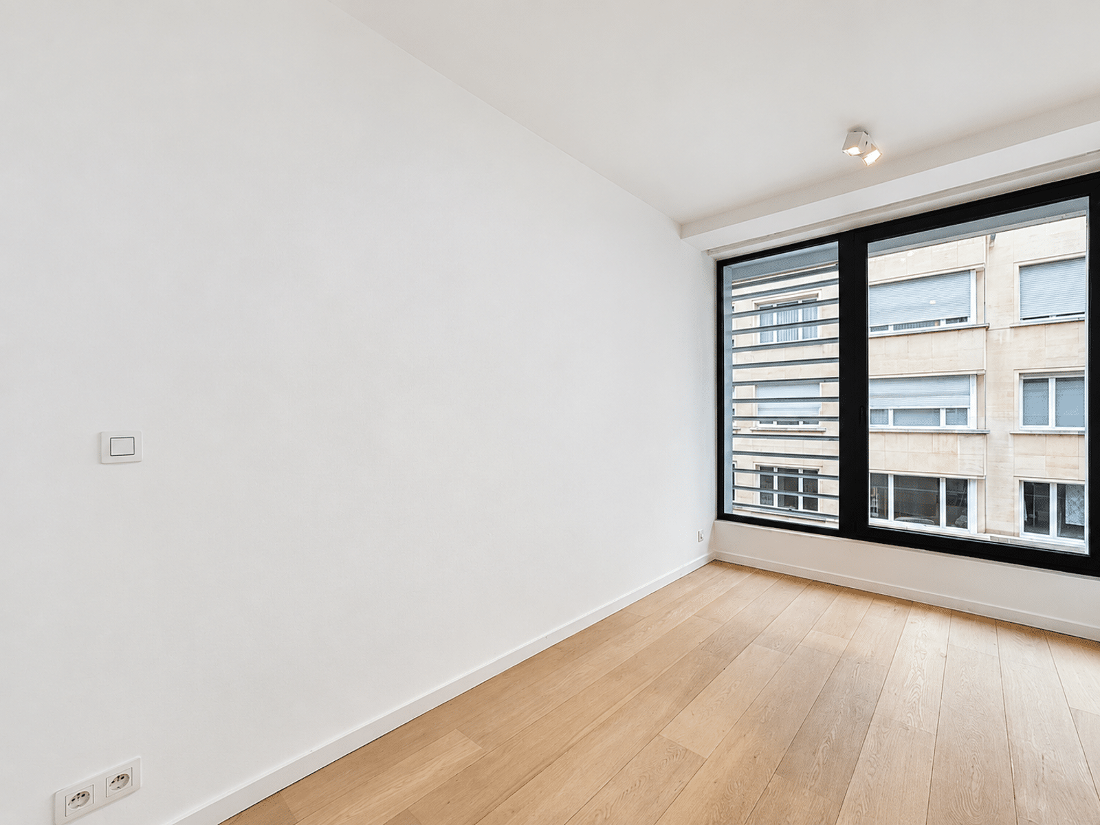Pièce Lumineuse avec Parquet Clair – You Real Estate Agency Pièce lumineuse d’appartement avec parquet clair et grande fenêtre noire.