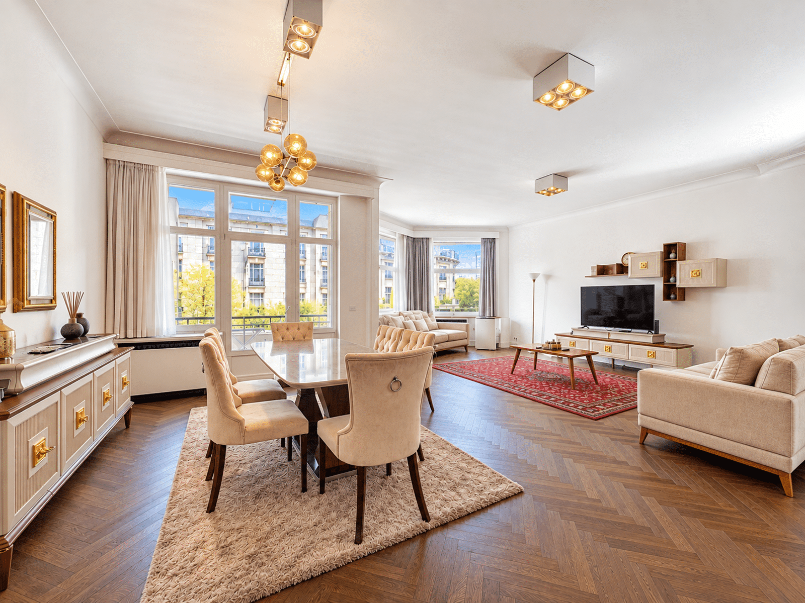 whise photo 3 Bright living room with beige sofas, a dining table, and large windows overlooking a cityscape.