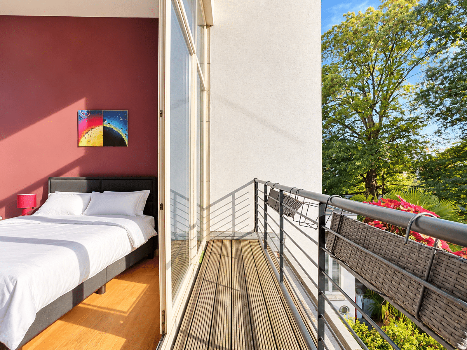 Chambre avec Balcon et Vue Verdoyante – You Real Estate Agency Chambre lumineuse d’appartement avec balcon en bois, fleurs et vue verdoyante.
