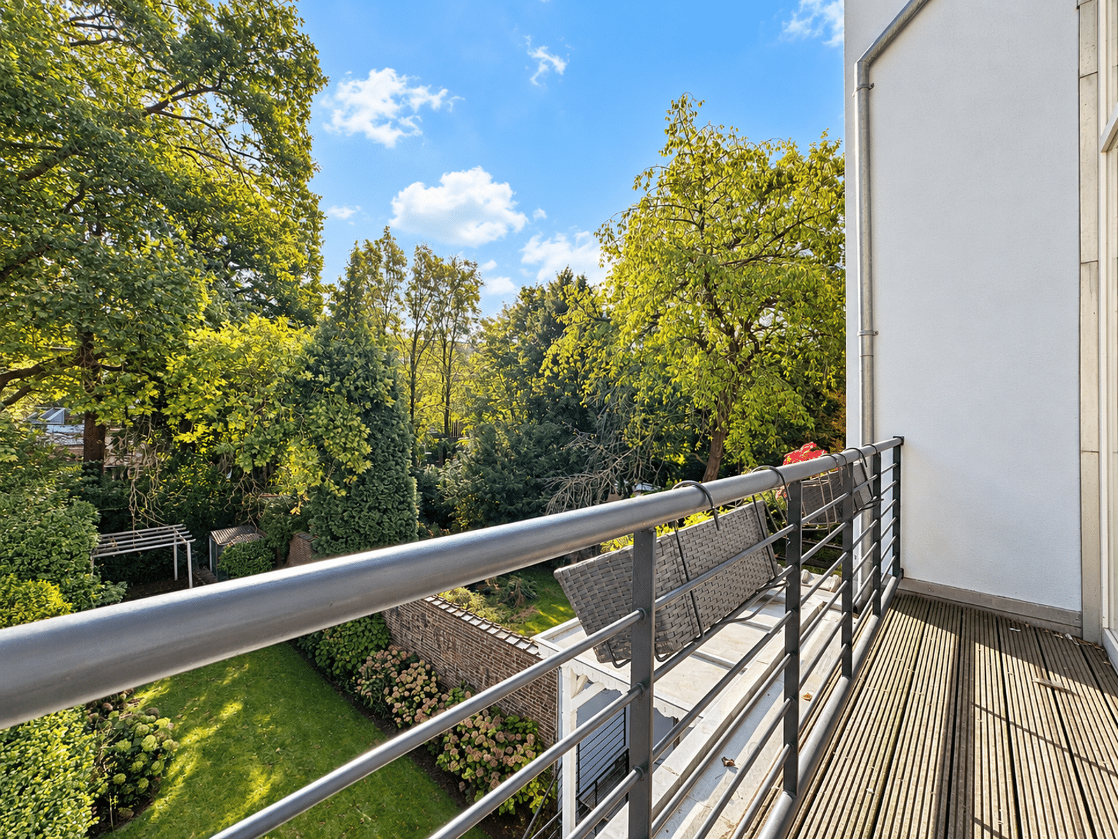 Balcon Avec Vue Sur Jardin – You Real Estate Agency Balcon d’appartement avec terrasse en bois et vue sur jardin arboré.