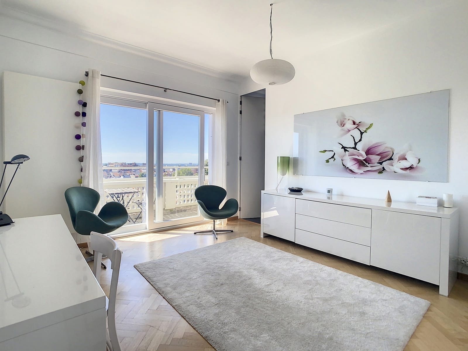 whise photo 12 Bright living room with white furniture, large glass doors to a balcony, and two green lounge chairs facing a light rug.