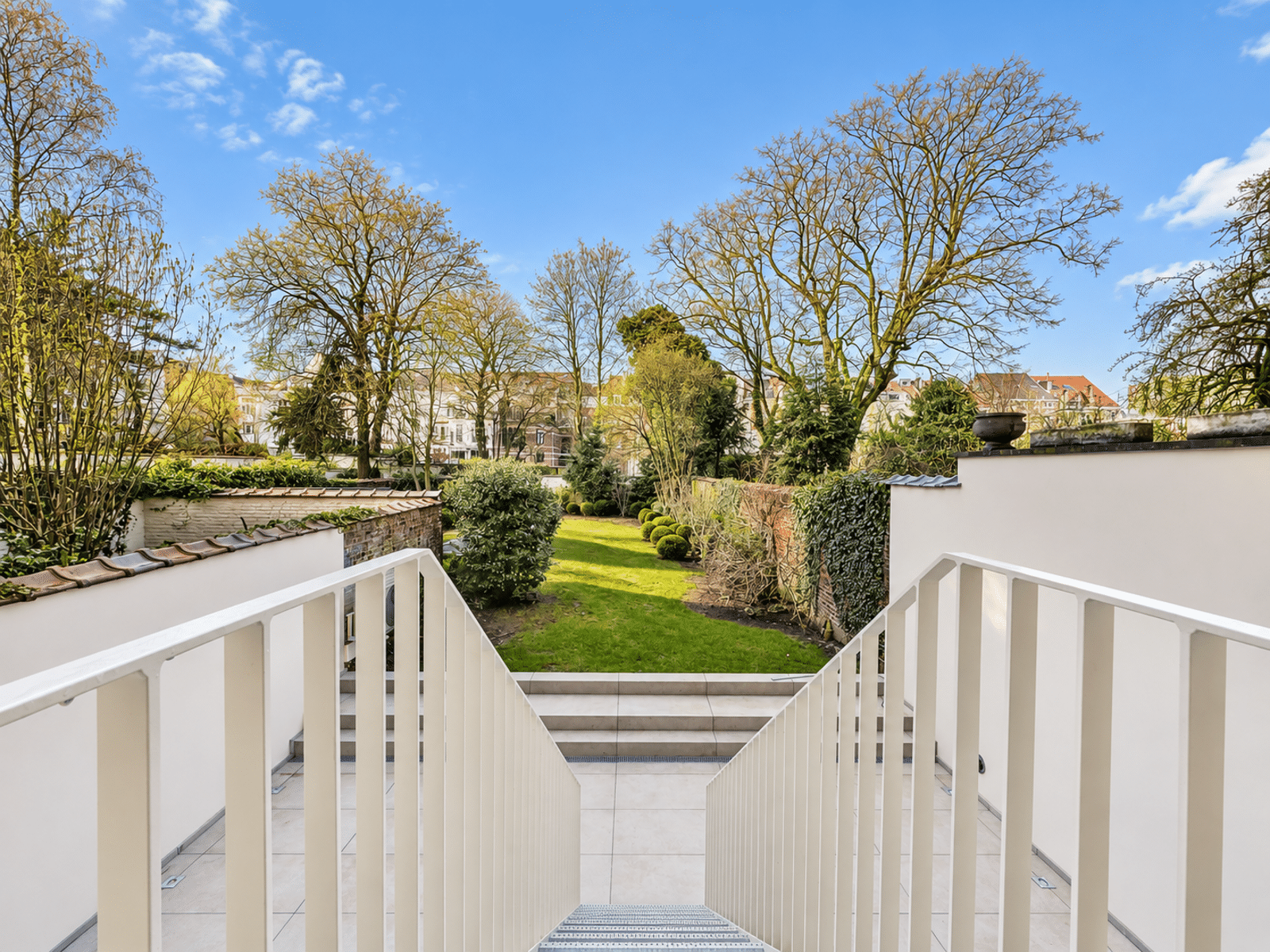 Jardin Paysager avec Terrasse – You Real Estate Agency Jardin paysager avec terrasse, pelouse et escaliers d’une maison.