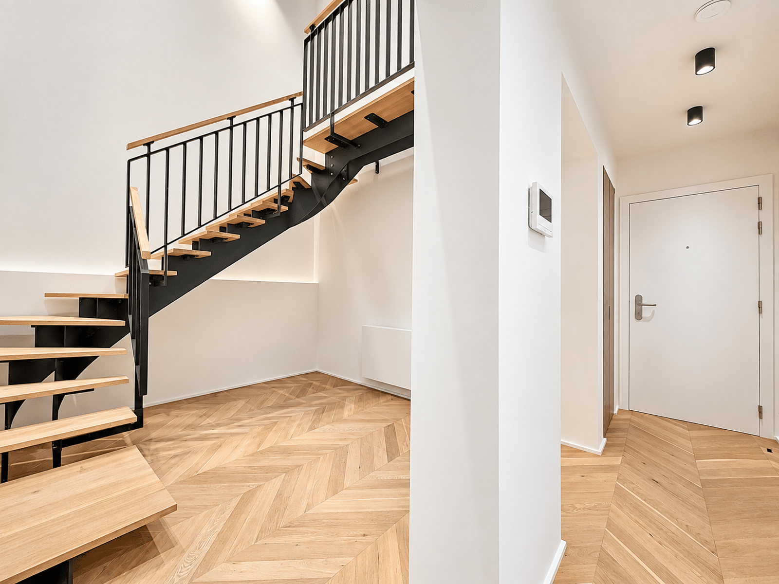whise photo 12 Modern interior staircase with black metal railing and light wood steps against white walls, in a bright hallway.