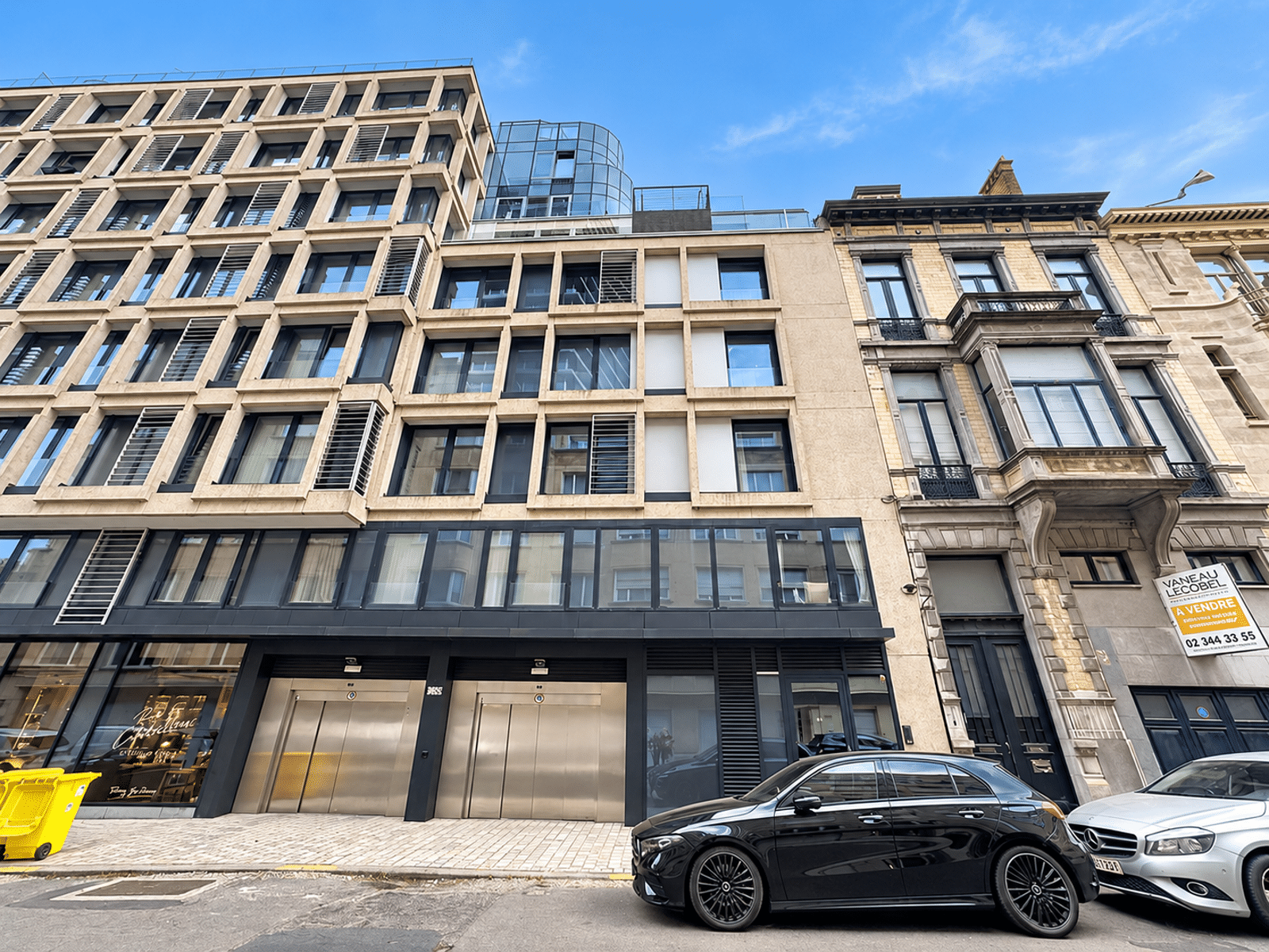 whise photo 12 Facade of a modern beige apartment building with grid of square windows and ground-floor storefronts under a blue sky